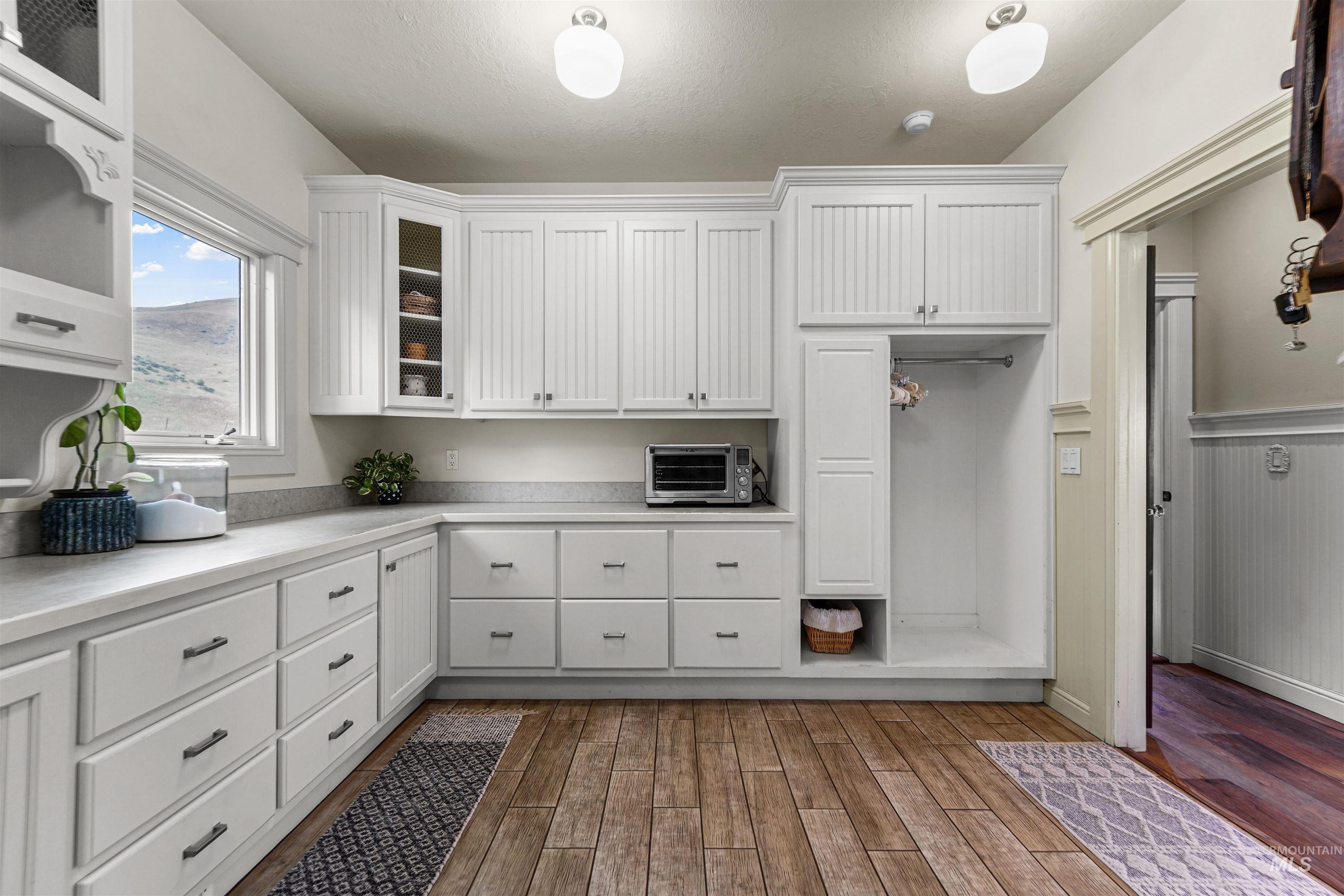 Kitchen featuring light countertops, dark wood-style floors, white cabinets, glass insert cabinets, and wainscoting