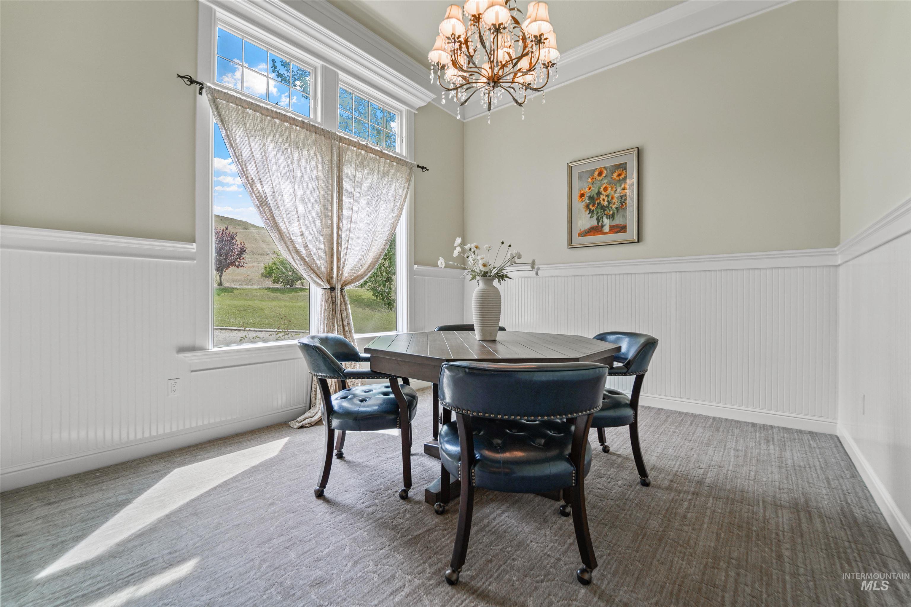 Carpeted dining room featuring a wainscoted wall, a chandelier, and ornamental molding
