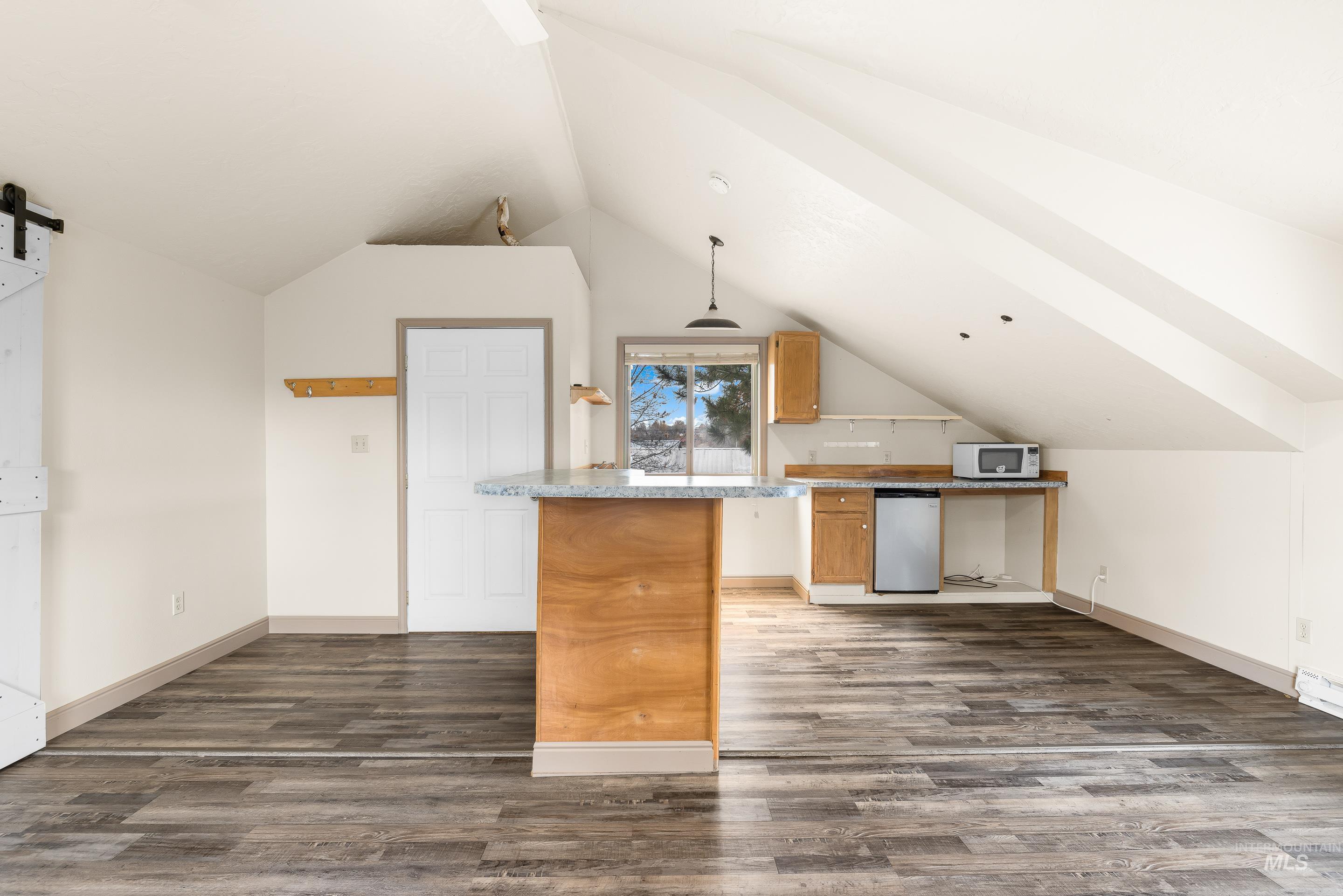 Kitchen featuring dishwasher, a barn door, decorative light fixtures, dark wood-type flooring, and vaulted ceiling