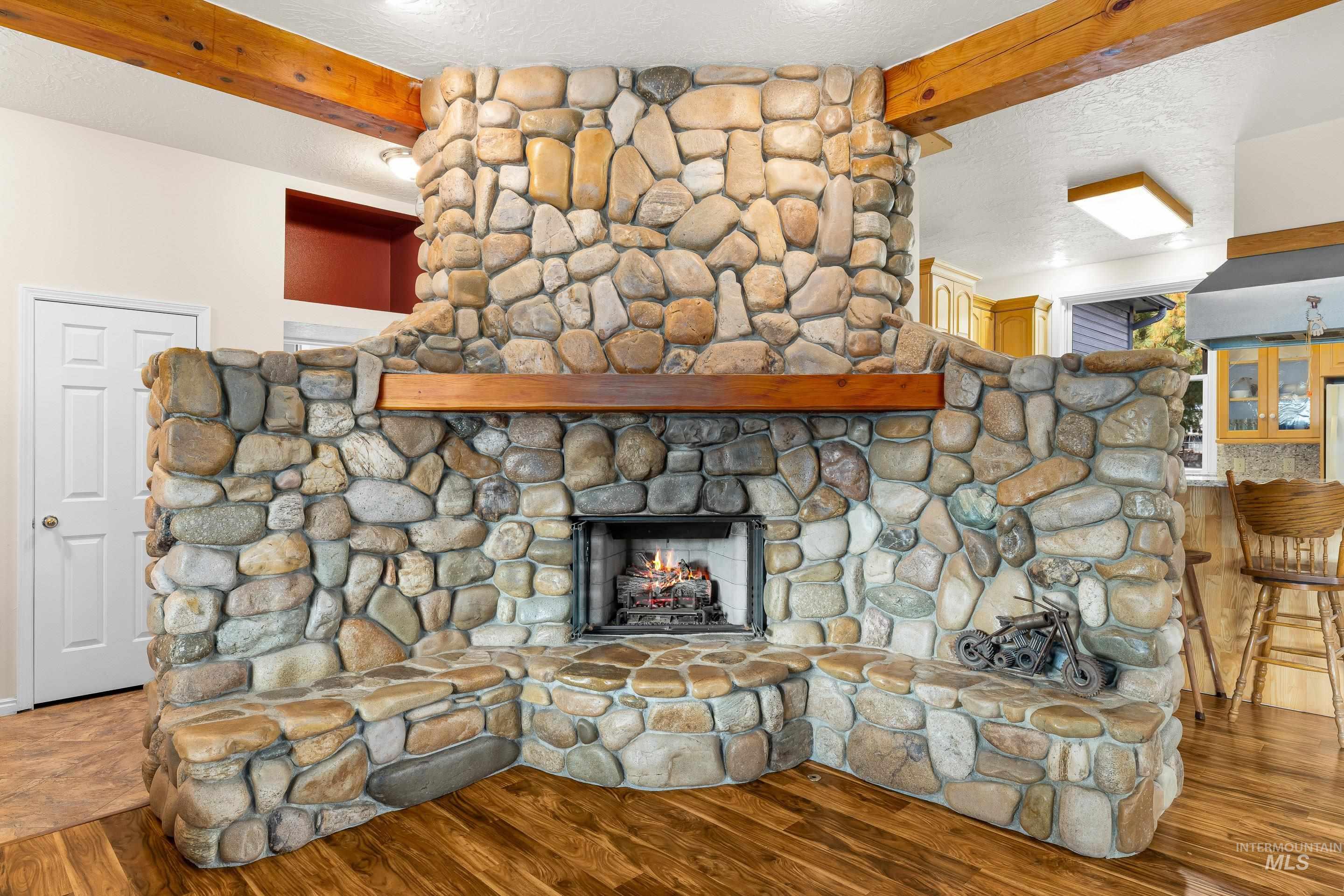 Detailed view of a fireplace, beam ceiling, wood finished floors, and a textured ceiling