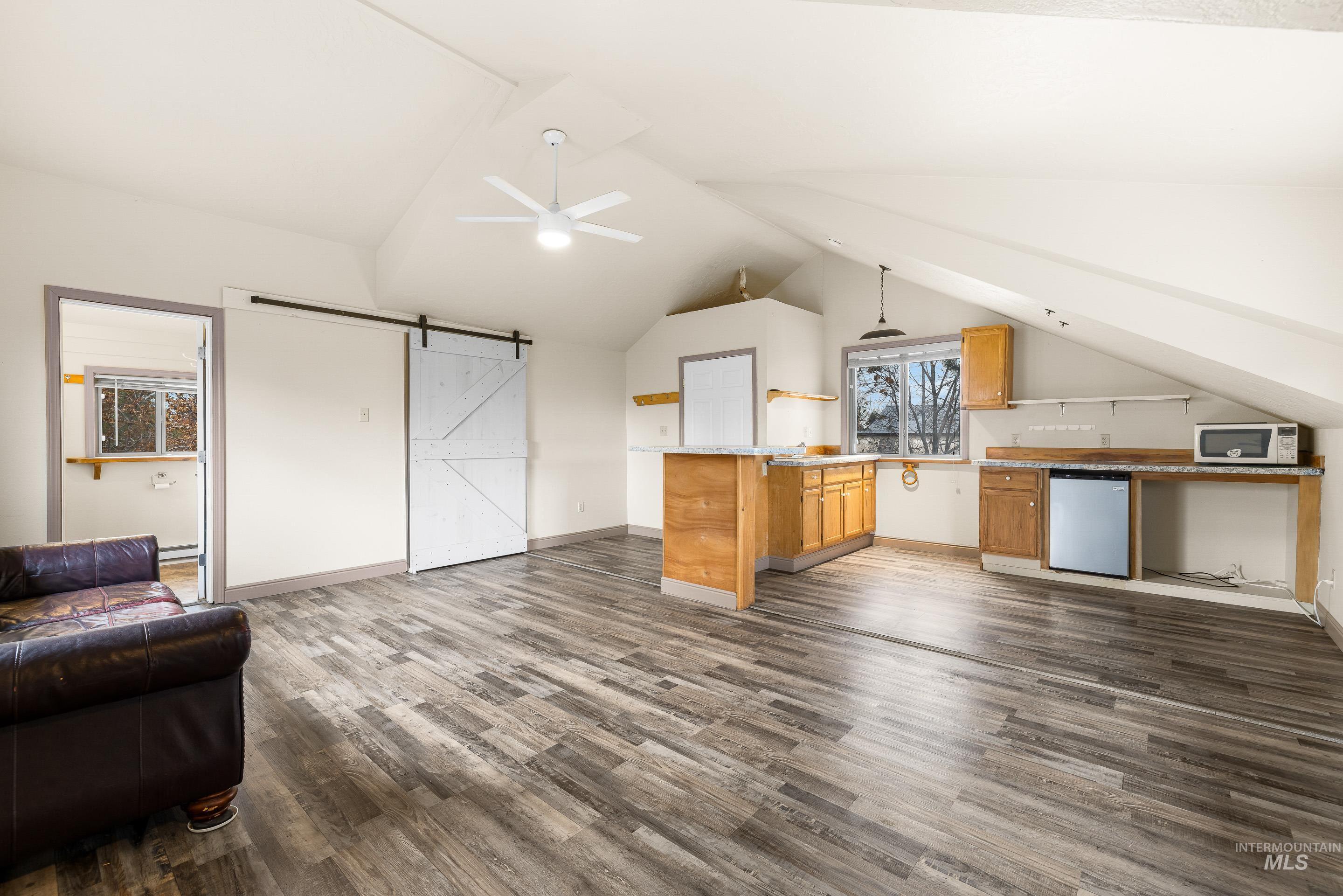 Bonus room with a barn door, lofted ceiling, a ceiling fan, and dark wood finished floors