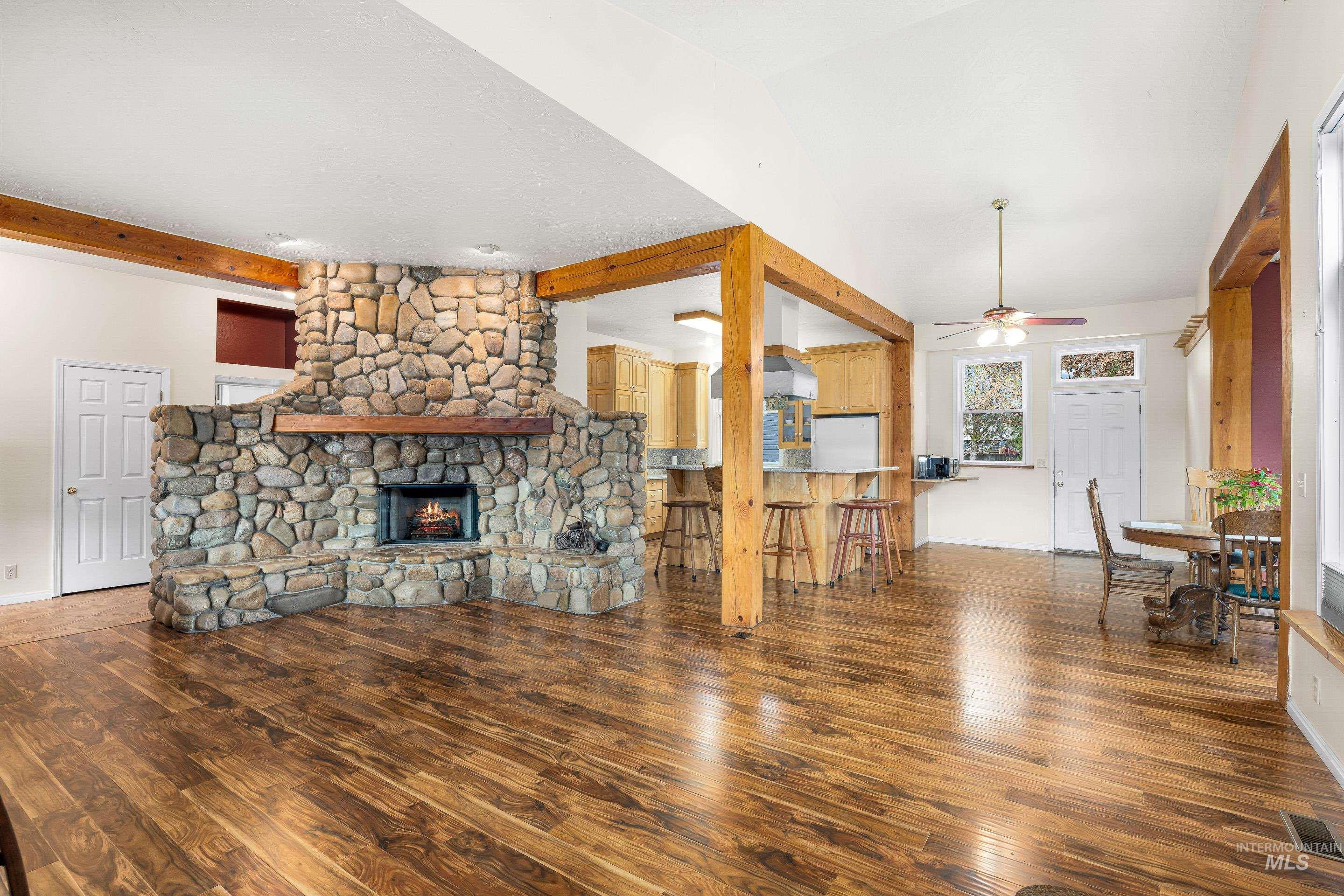Living area with beam ceiling, a stone fireplace, ceiling fan, and dark wood-type flooring