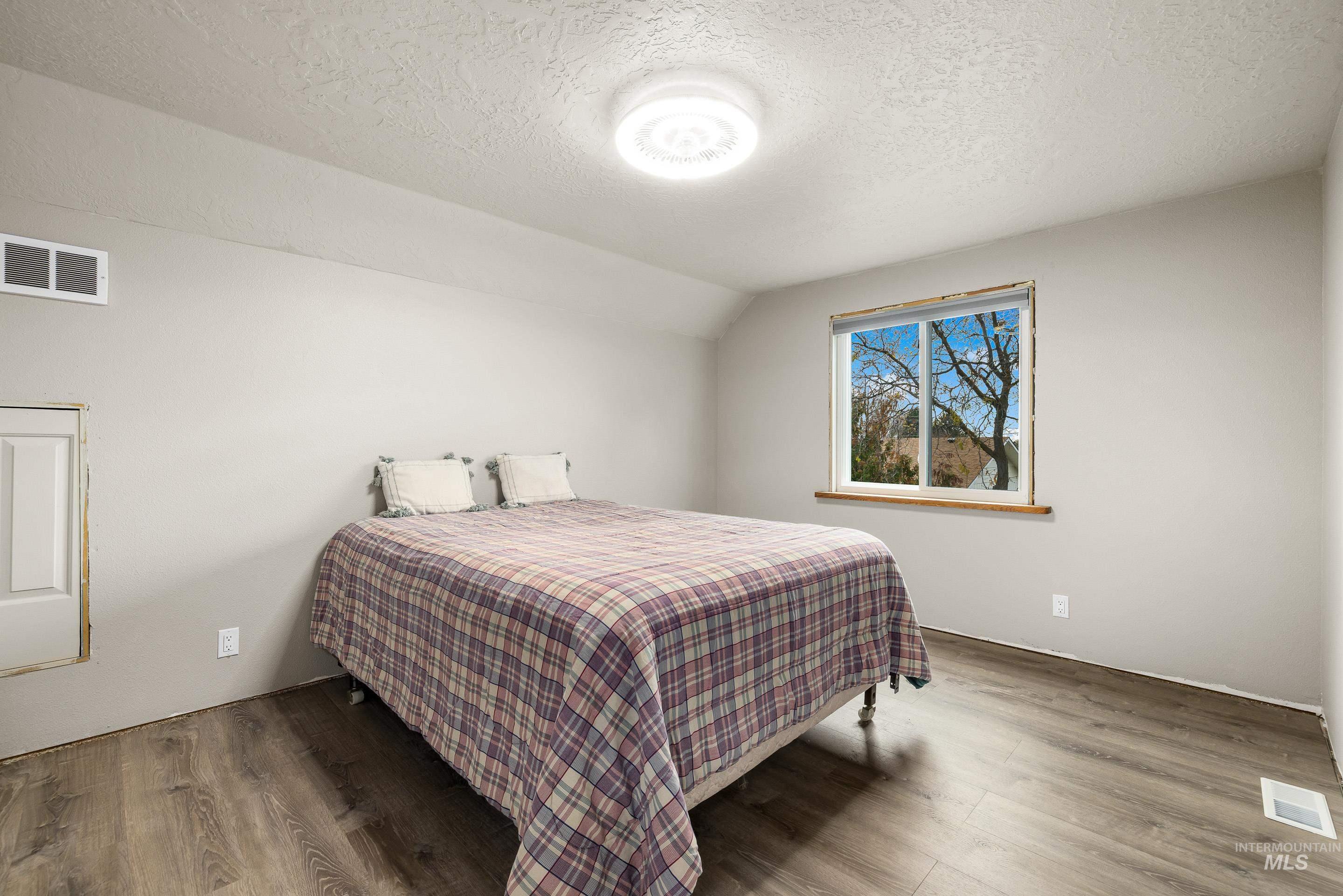 Bedroom featuring a textured ceiling, vaulted ceiling, and wood finished floors