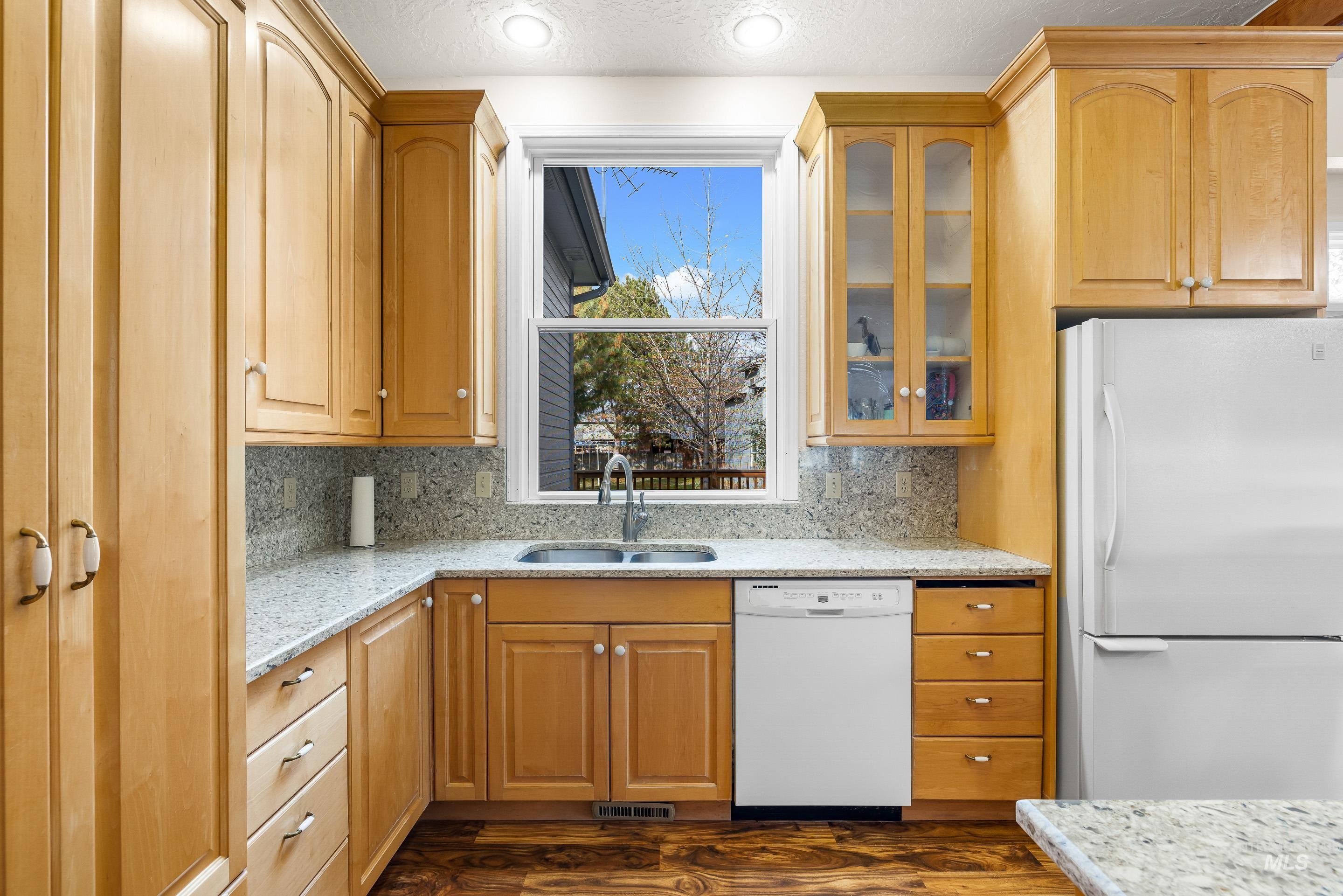 Kitchen with white appliances, light stone countertops, tasteful backsplash, glass insert cabinets, and a textured ceiling