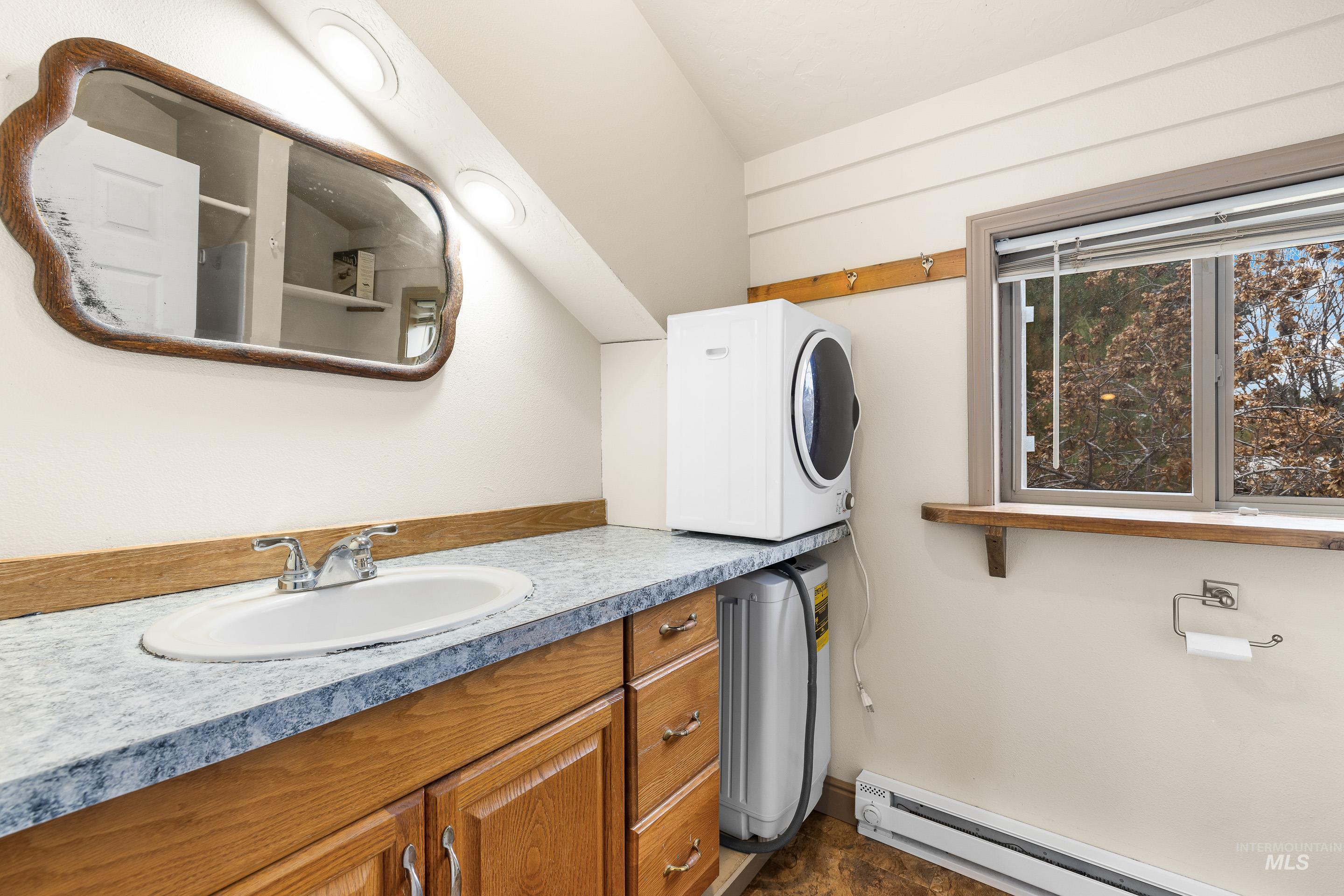 Bathroom featuring a baseboard heating unit, stacked washer / drying machine, and vanity