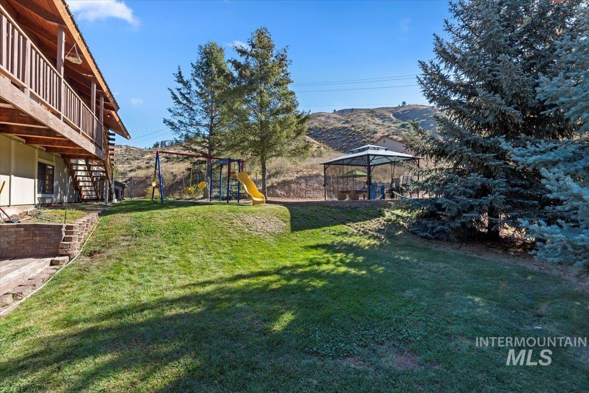 View of grassy yard featuring a playground, stairway, a patio, and a deck with mountain view
