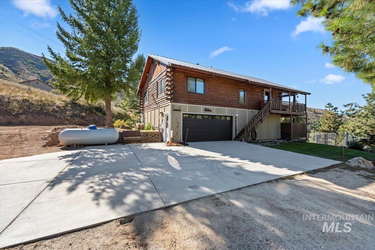 Log-style house with log exterior, stairs, driveway, a garage, and a metal roof