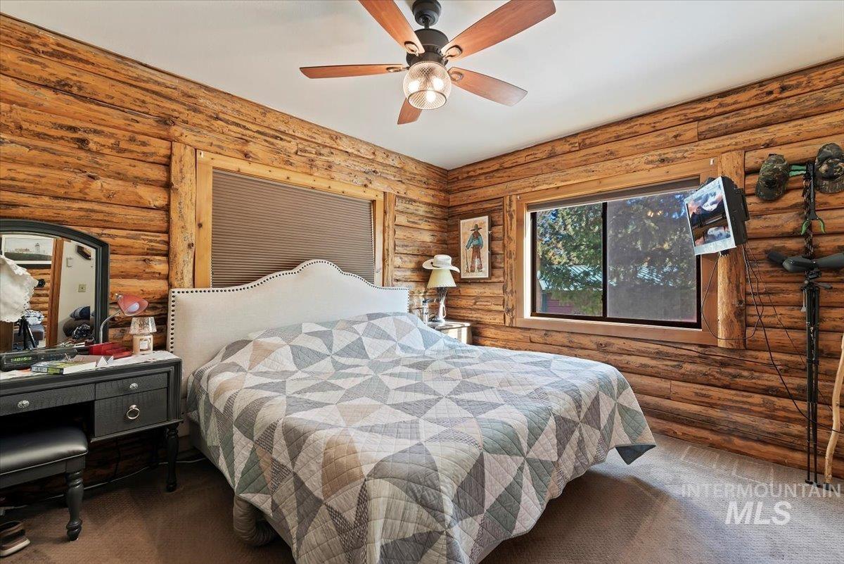 Bedroom with carpet flooring, rustic walls, and a ceiling fan