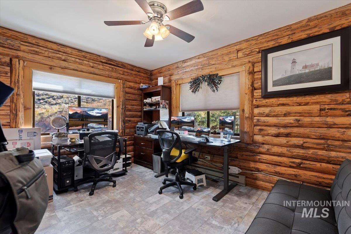 Office space with baseboard heating, rustic walls, and a ceiling fan