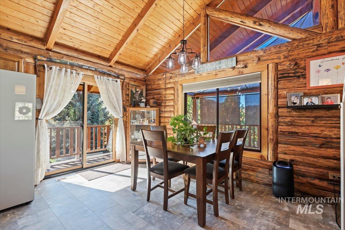 Dining room featuring rustic walls, a wooden ceiling with exposed beams, and high vaulted ceiling