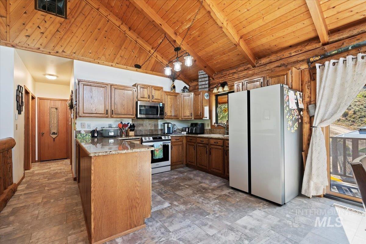 Kitchen with stainless steel appliances, brown cabinets, a wooden ceiling with exposed beams, light stone counters, and high vaulted ceiling
