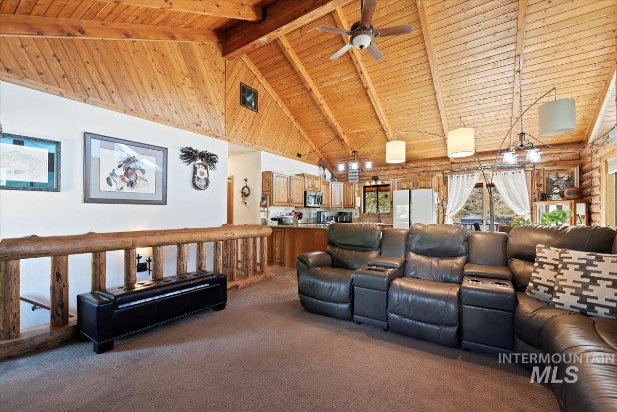 Living area with high vaulted ceiling, dark carpet, a wooden ceiling with exposed beams, ceiling fan, and rustic walls