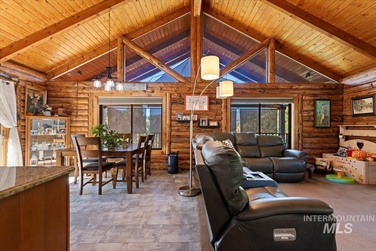 Living area with rustic walls, healthy amount of natural light, high vaulted ceiling, and a wooden ceiling with exposed beams