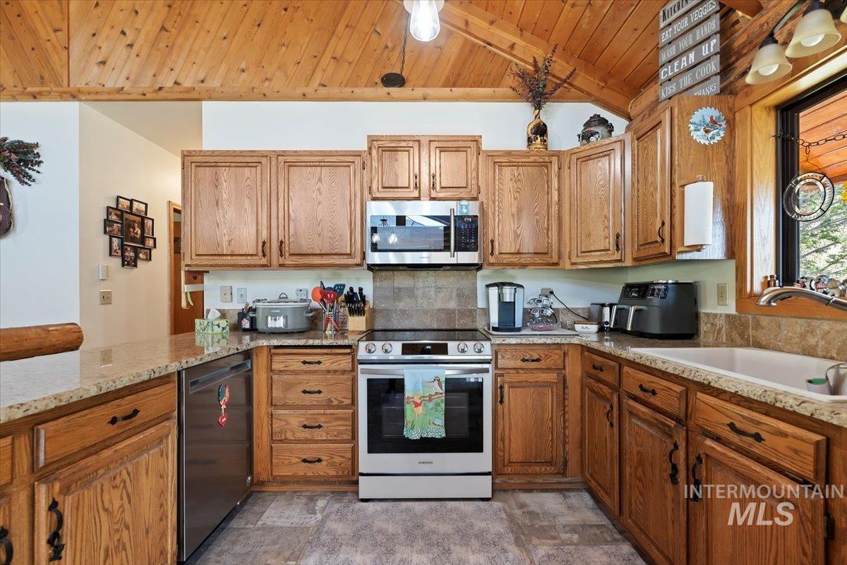 Kitchen featuring stainless steel appliances, brown cabinets, light stone counters, wood ceiling, and decorative backsplash