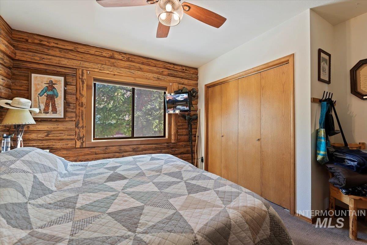 Carpeted bedroom featuring a closet, log walls, and a ceiling fan