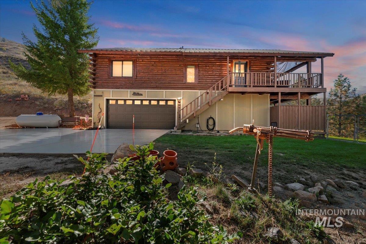 Log cabin featuring stairs, concrete driveway, log siding, a front lawn, and a deck