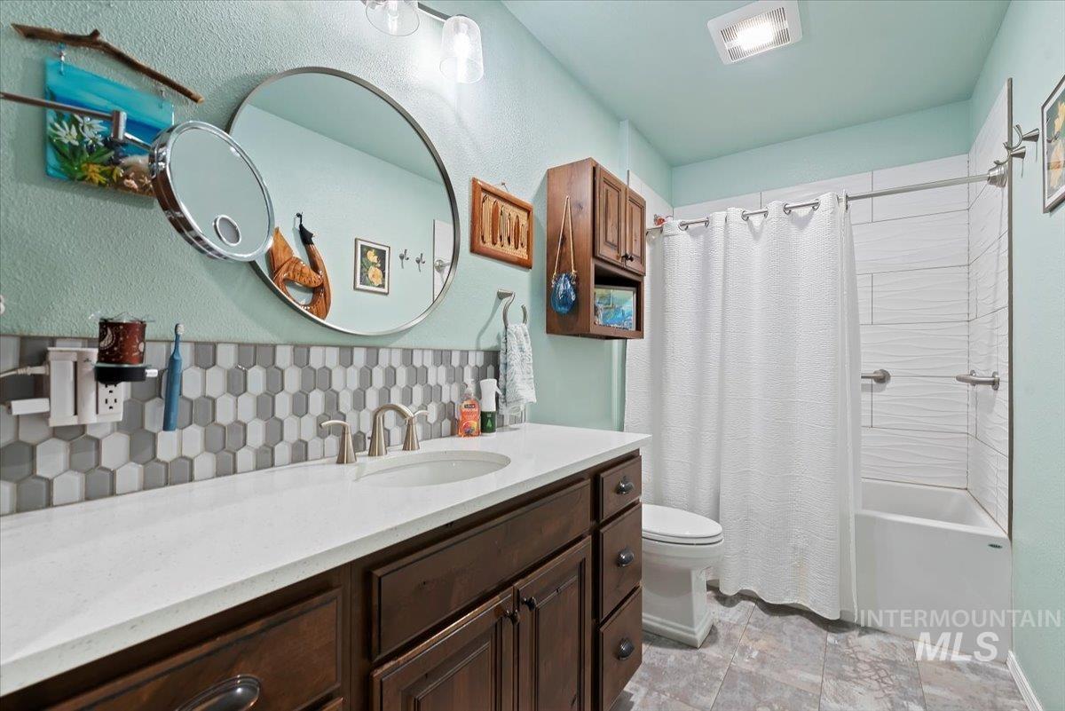 Full bath featuring shower / bath combo, vanity, backsplash, light stone finish floors, and a textured wall