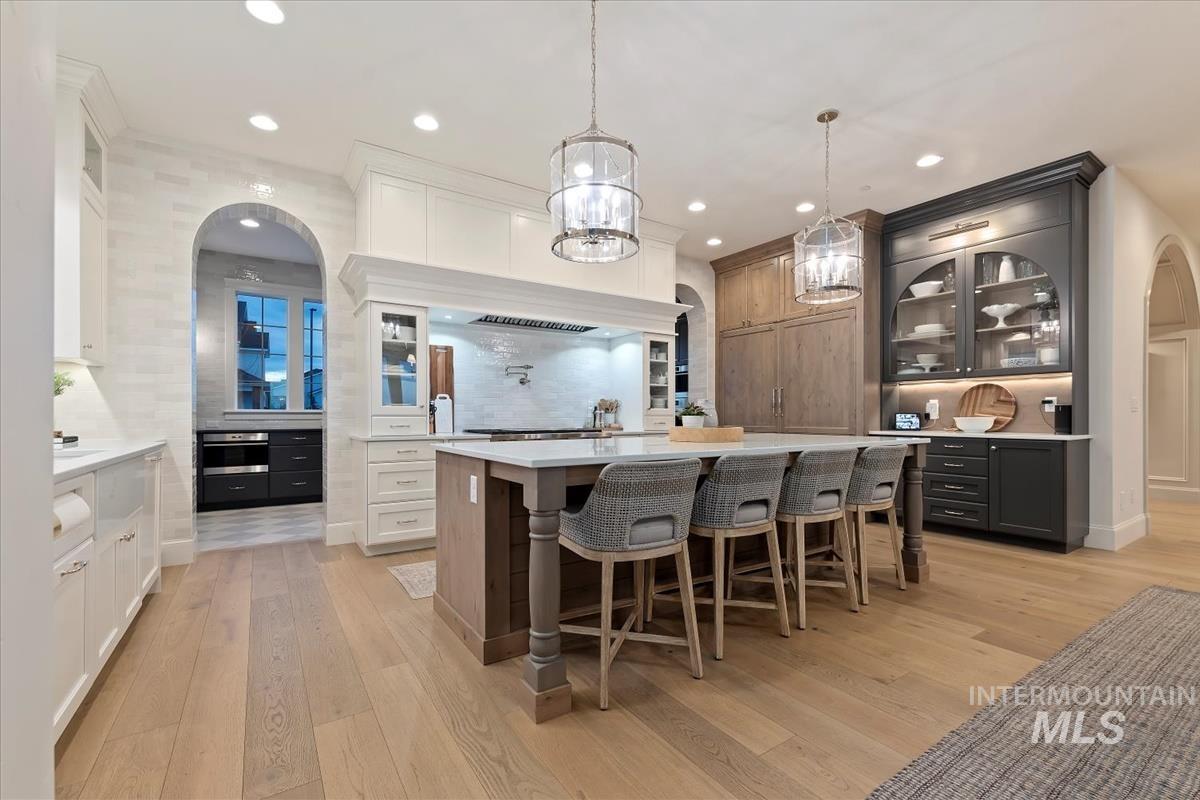 Dual tone kitchen featuring arched walkways, glass insert cabinets, two tone color scheme, light wood finished floors, and a kitchen breakfast bar