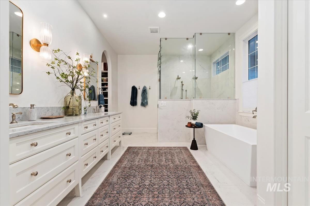 Bathroom with a freestanding tub, double vanity, recessed lighting, a marble finish shower, and light marble finish floors