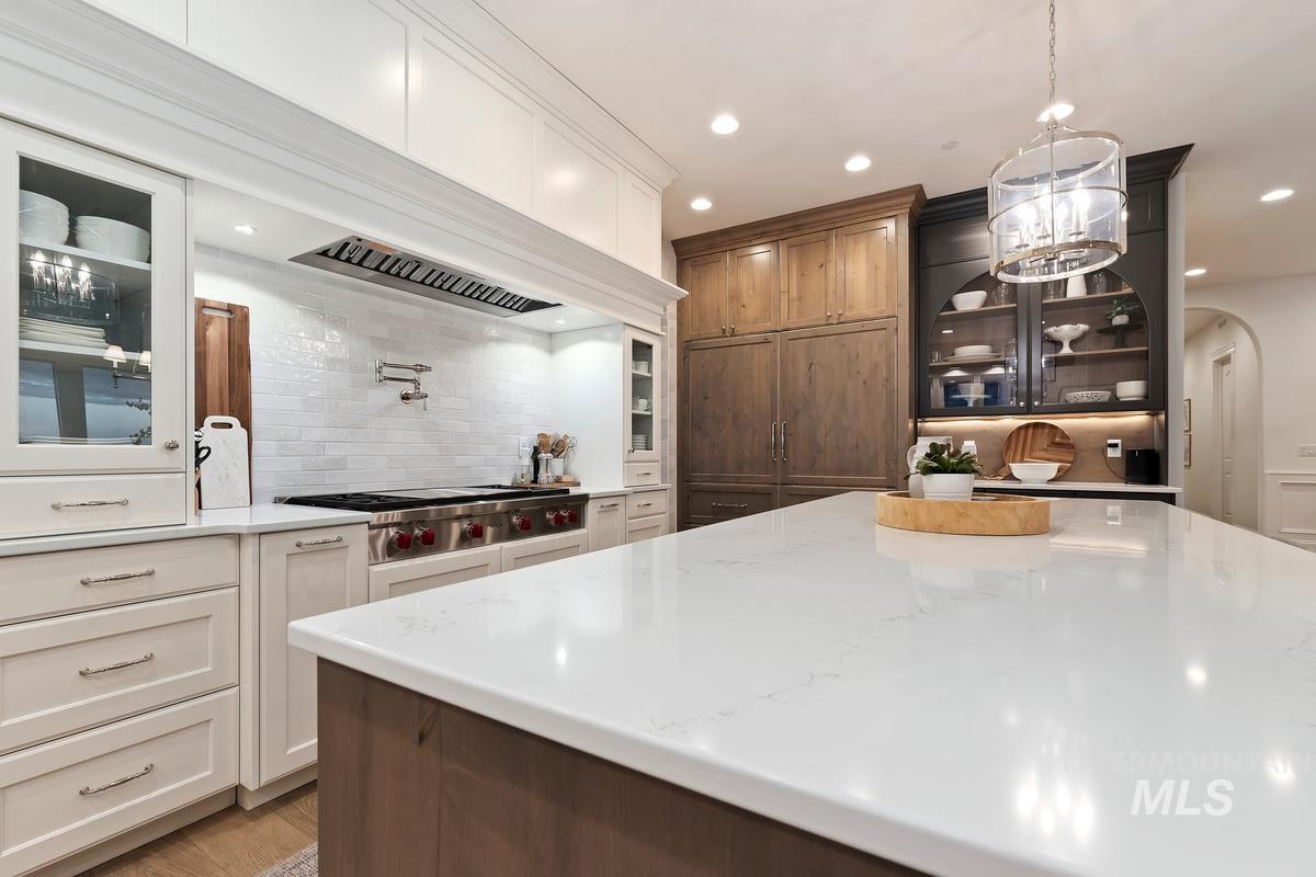 Two tone kitchen featuring glass fronted cabinets, two tone color scheme, light stone countertops, stainless steel gas cooktop, and arched walkways