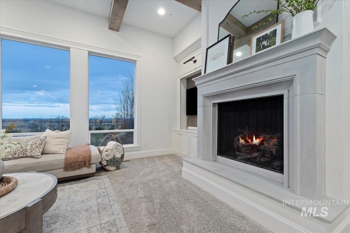Living area with a lit fireplace, light colored carpet, and beam ceiling