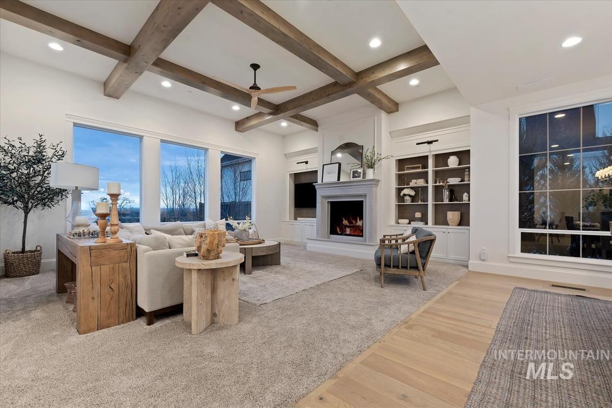 Living area with ceiling fan, built in shelves, a lit fireplace, light wood-type flooring, and coffered ceiling