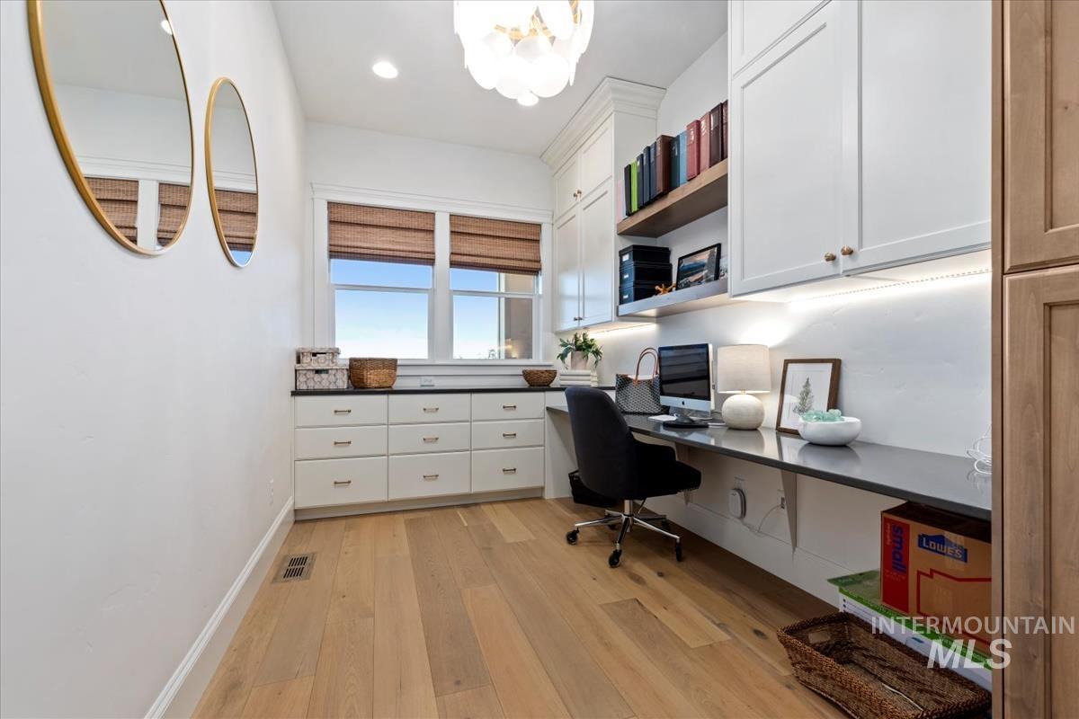 Home office featuring built in desk, light wood finished floors, and hanging lights