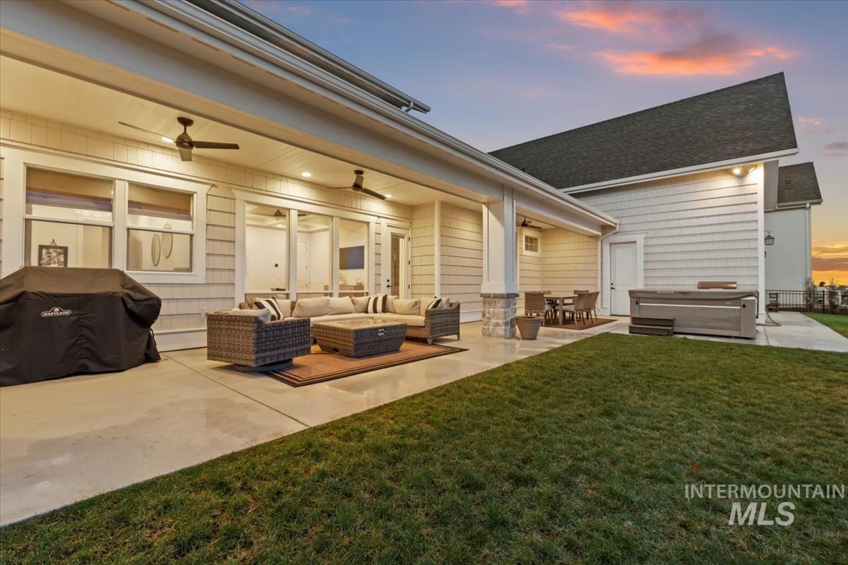 Back of property at dusk featuring ceiling fan, outdoor lounge area, a hot tub, a patio area, and a lawn