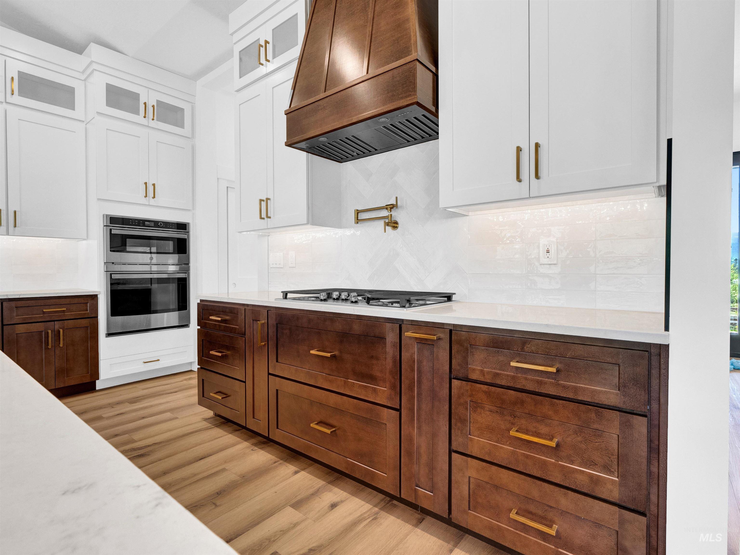 Kitchen with light wood-style floors, white cabinets, premium range hood, and backsplash