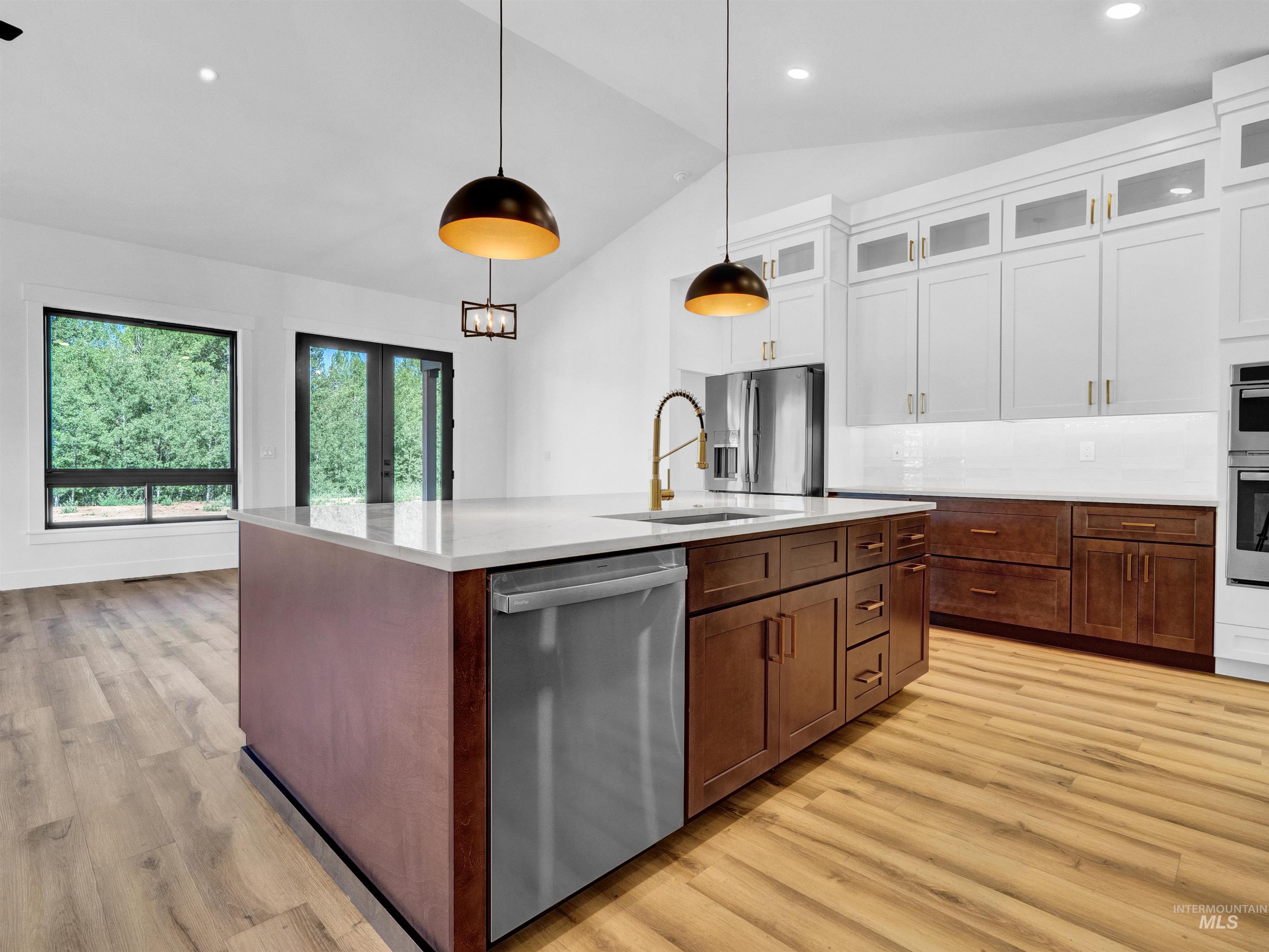 Kitchen featuring vaulted ceiling, stainless steel appliances, light countertops, white cabinets, and light wood-style flooring