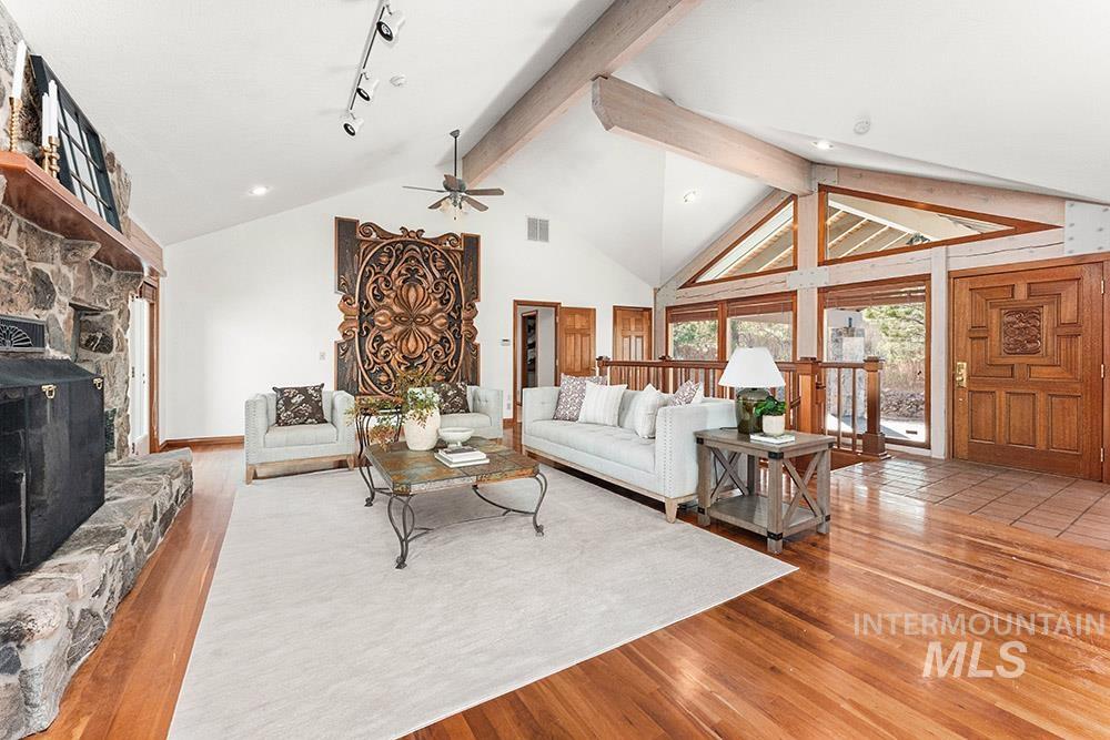 Living room featuring wood finished floors, ceiling fan, beam ceiling, a fireplace, and high vaulted ceiling