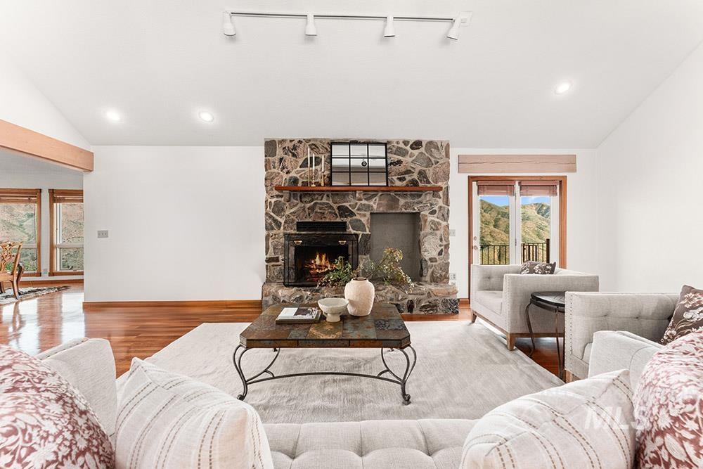 Living area featuring vaulted ceiling, wood finished floors, and a stone fireplace