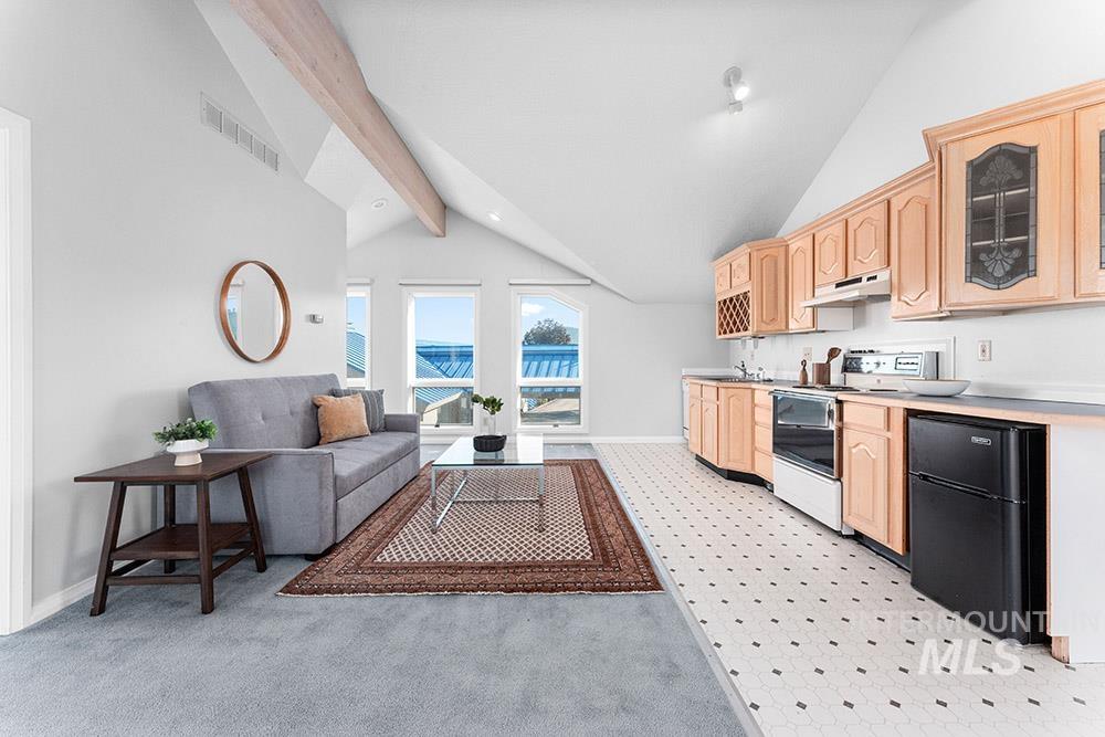Kitchen with light brown cabinetry, white electric range, freestanding refrigerator, glass insert cabinets, and light countertops
