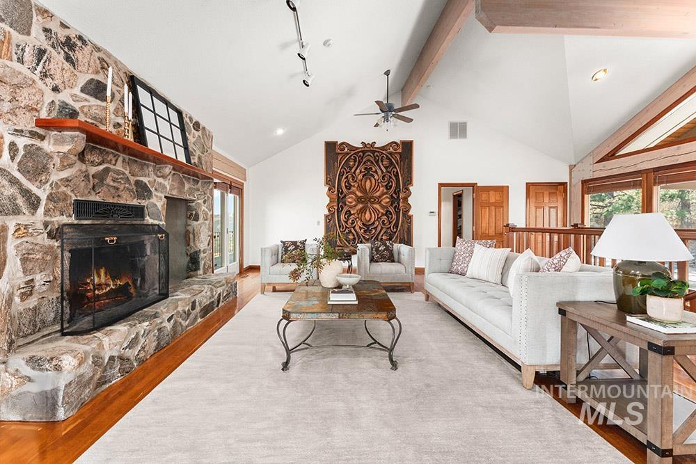 Living area with ceiling fan, high vaulted ceiling, a stone fireplace, wood finished floors, and beam ceiling
