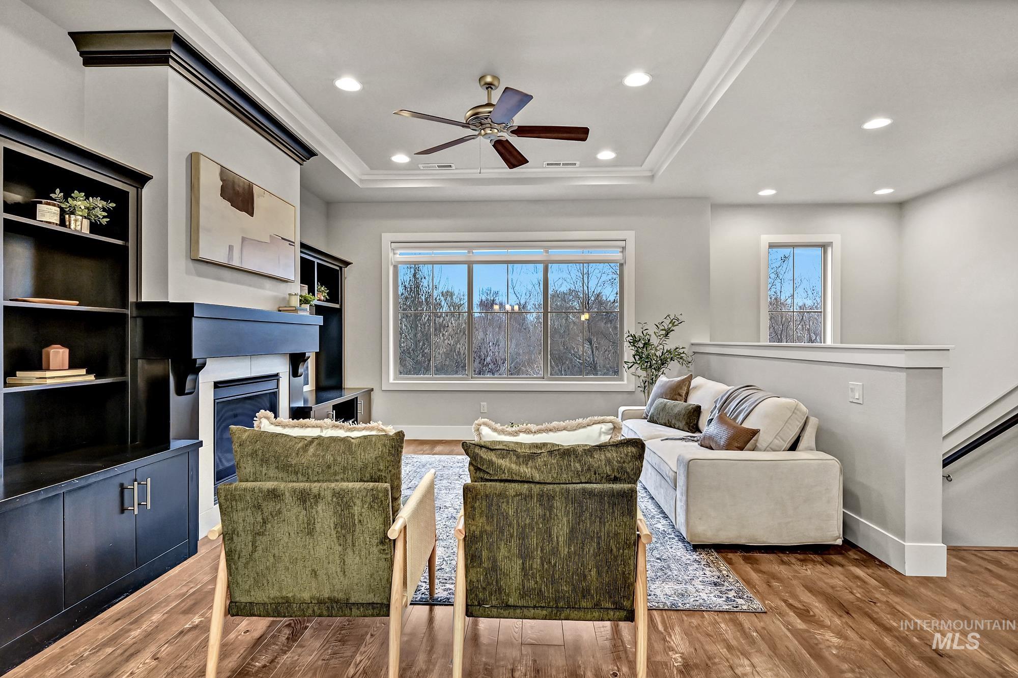 Living area featuring a gas fireplace insert, wood floors, a tray ceiling, a ceiling fan, and recessed lighting