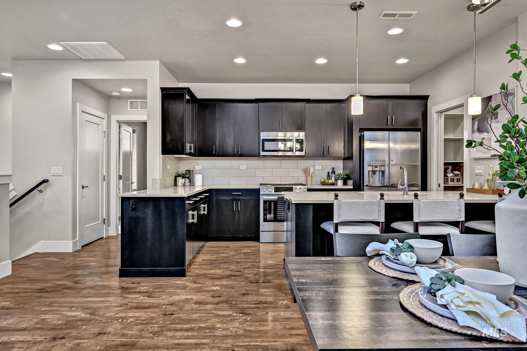 Kitchen featuring an island, appliances with stainless steel finishes, pendant light fixtures, tasteful tile backsplash, and dark wood-style flooring