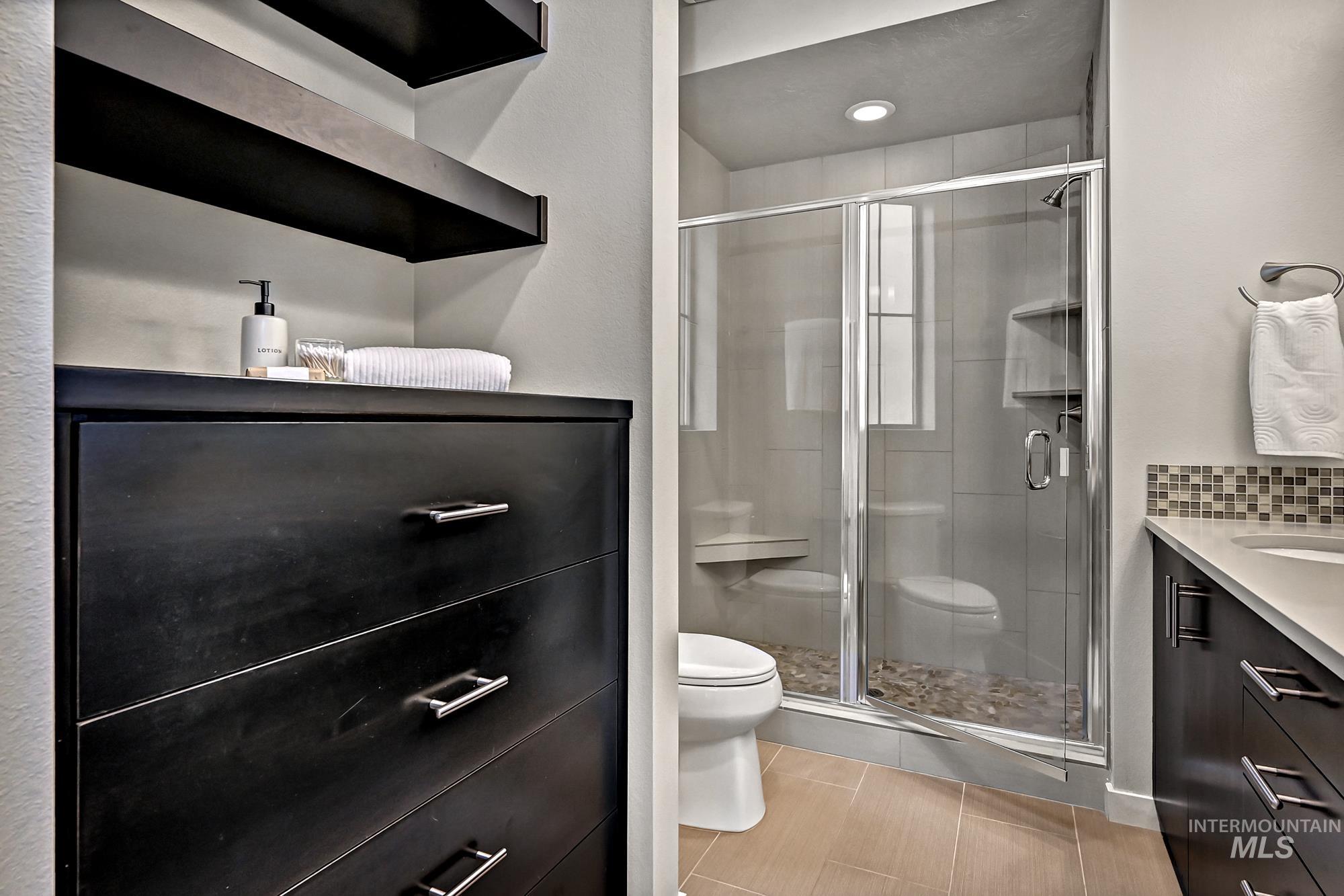 Full bathroom with vanity, a stall shower, and light tile patterned flooring plus a built-in cabinet for storage.