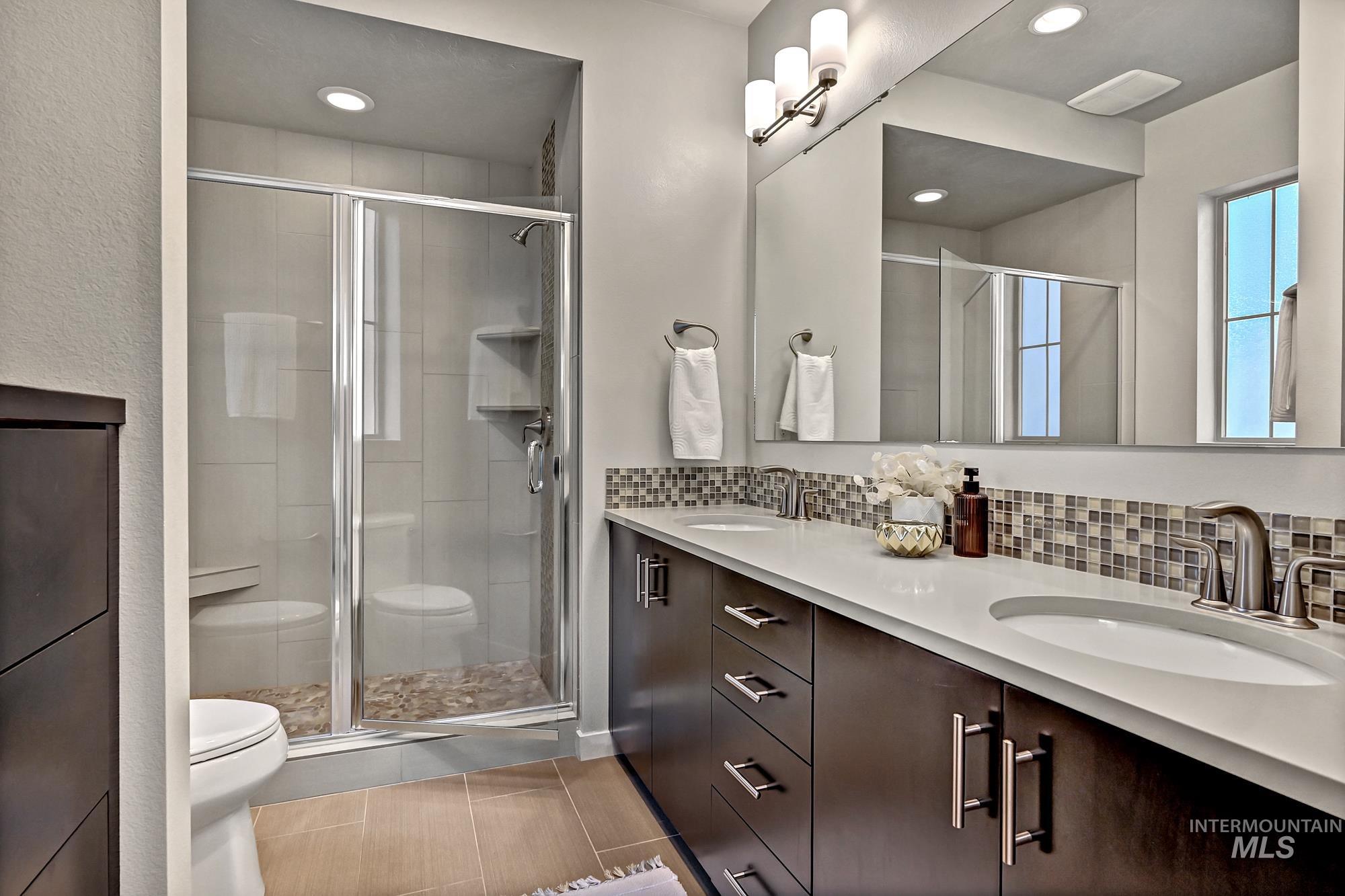 Full bathroom with double vanity, a stall shower, backsplash, light tile patterned floors, and recessed lighting