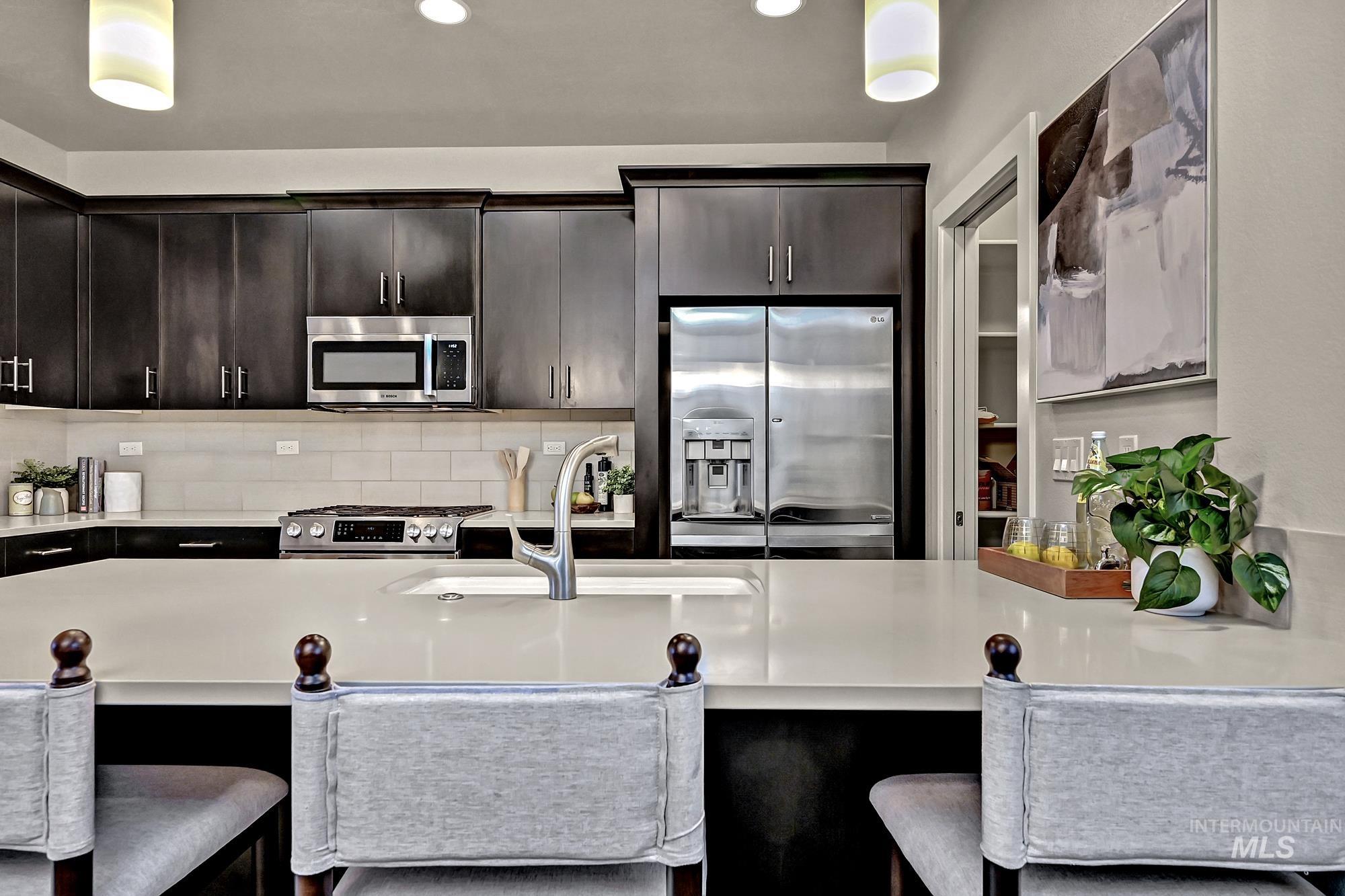 Kitchen featuring an island, appliances with stainless steel finishes, pendant light fixtures, tasteful tile backsplash, and dark wood-style flooring