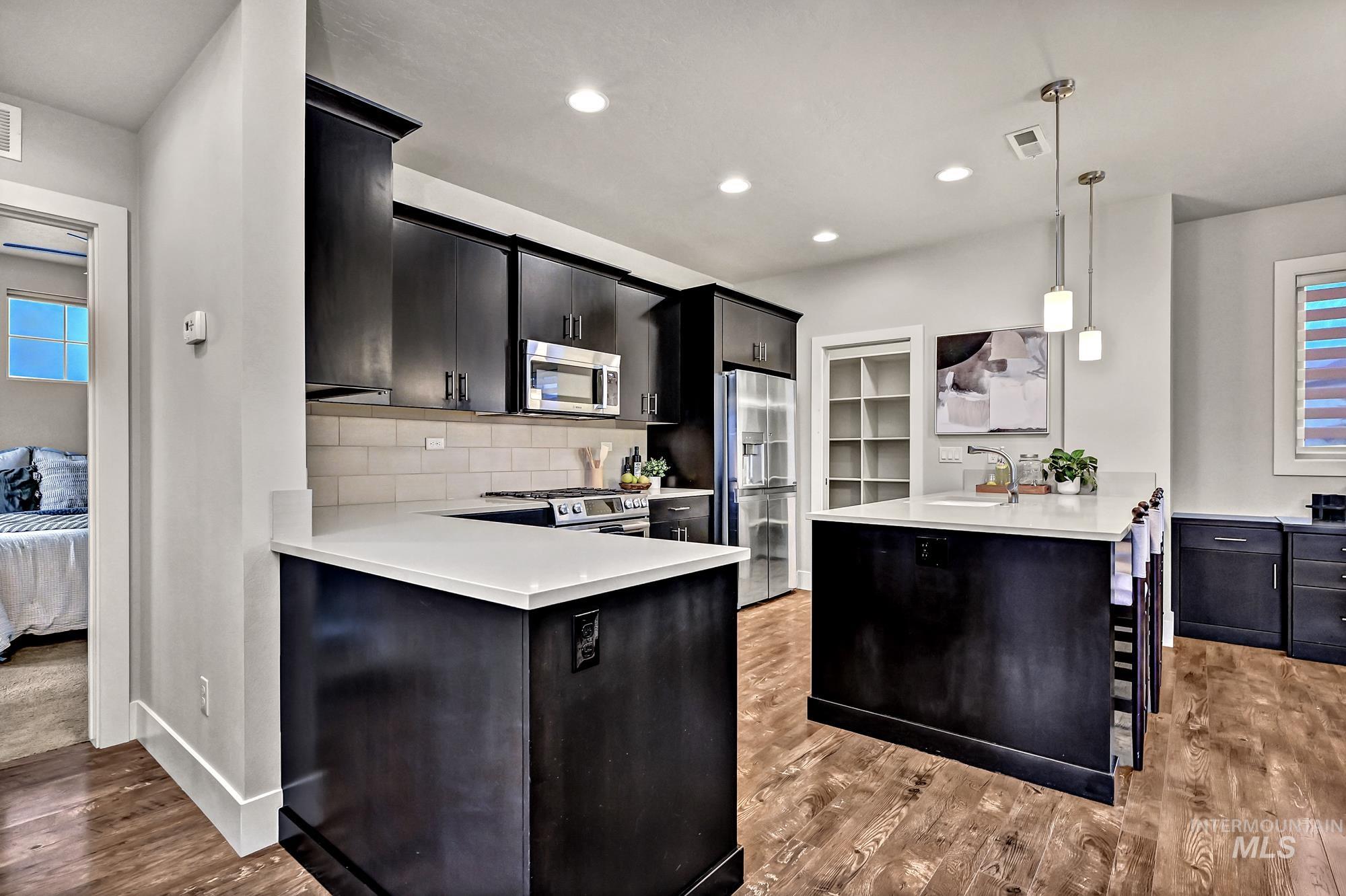 Kitchen featuring a peninsula, an island, plenty of natural light, decorative pendant light fixtures, dark cabinets, and recessed lighting