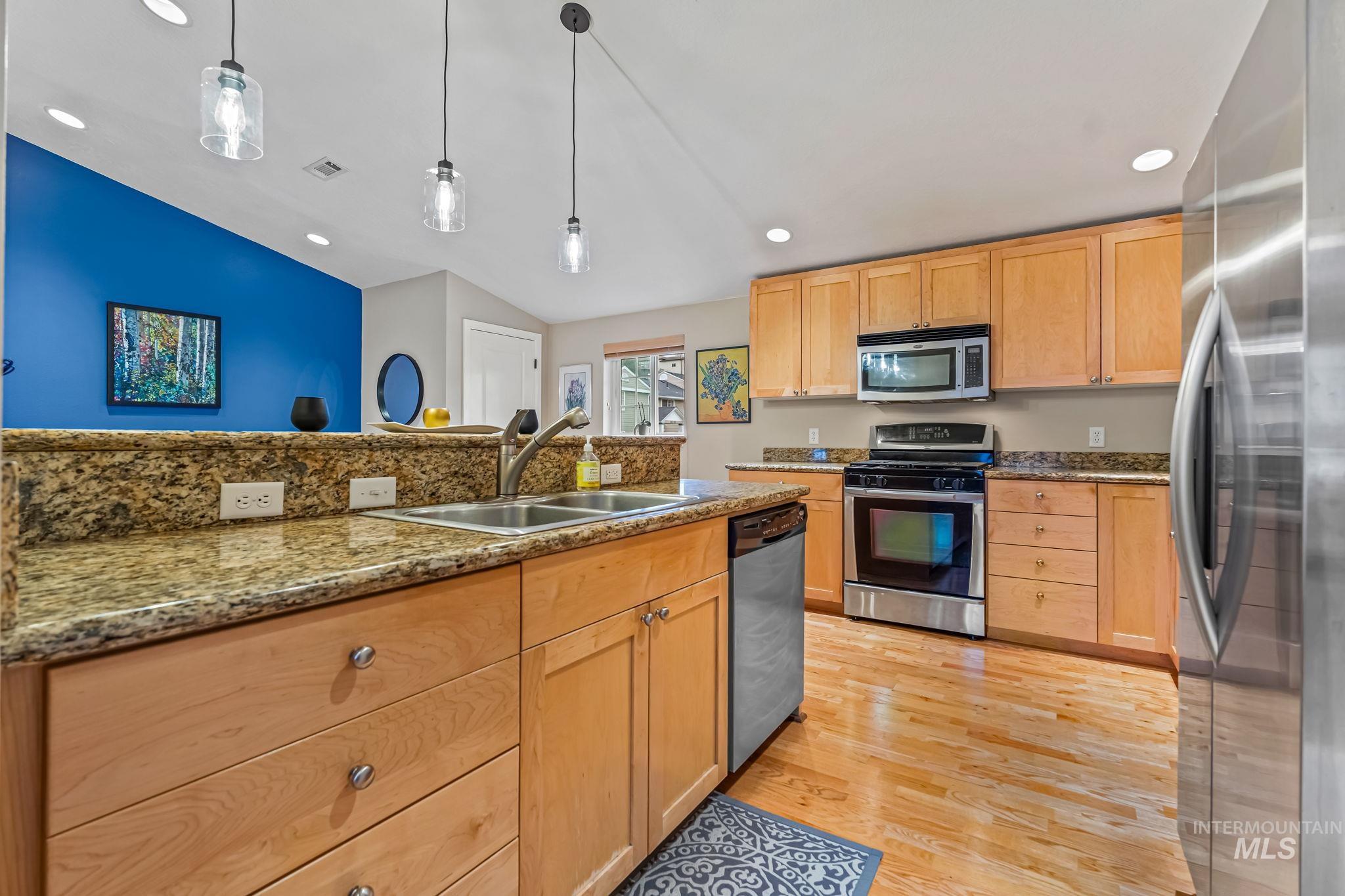 Kitchen featuring stainless steel appliances, vaulted ceiling, light wood finish cabinets, granite countertops, and new hanging light fixtures