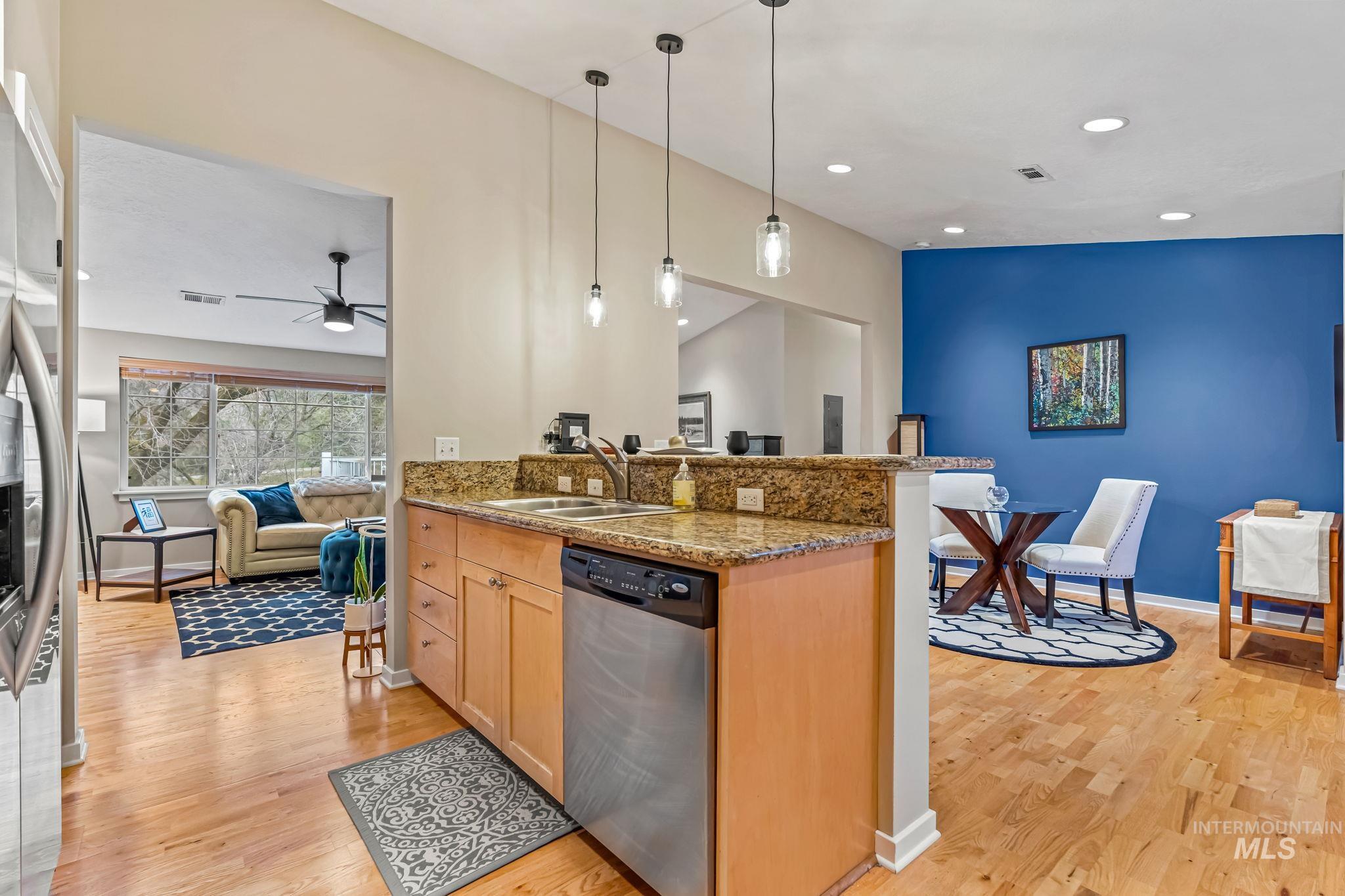 Kitchen with open floor plan, stainless steel appliances, granite counters, light hardwood floors, and new hanging light fixtures