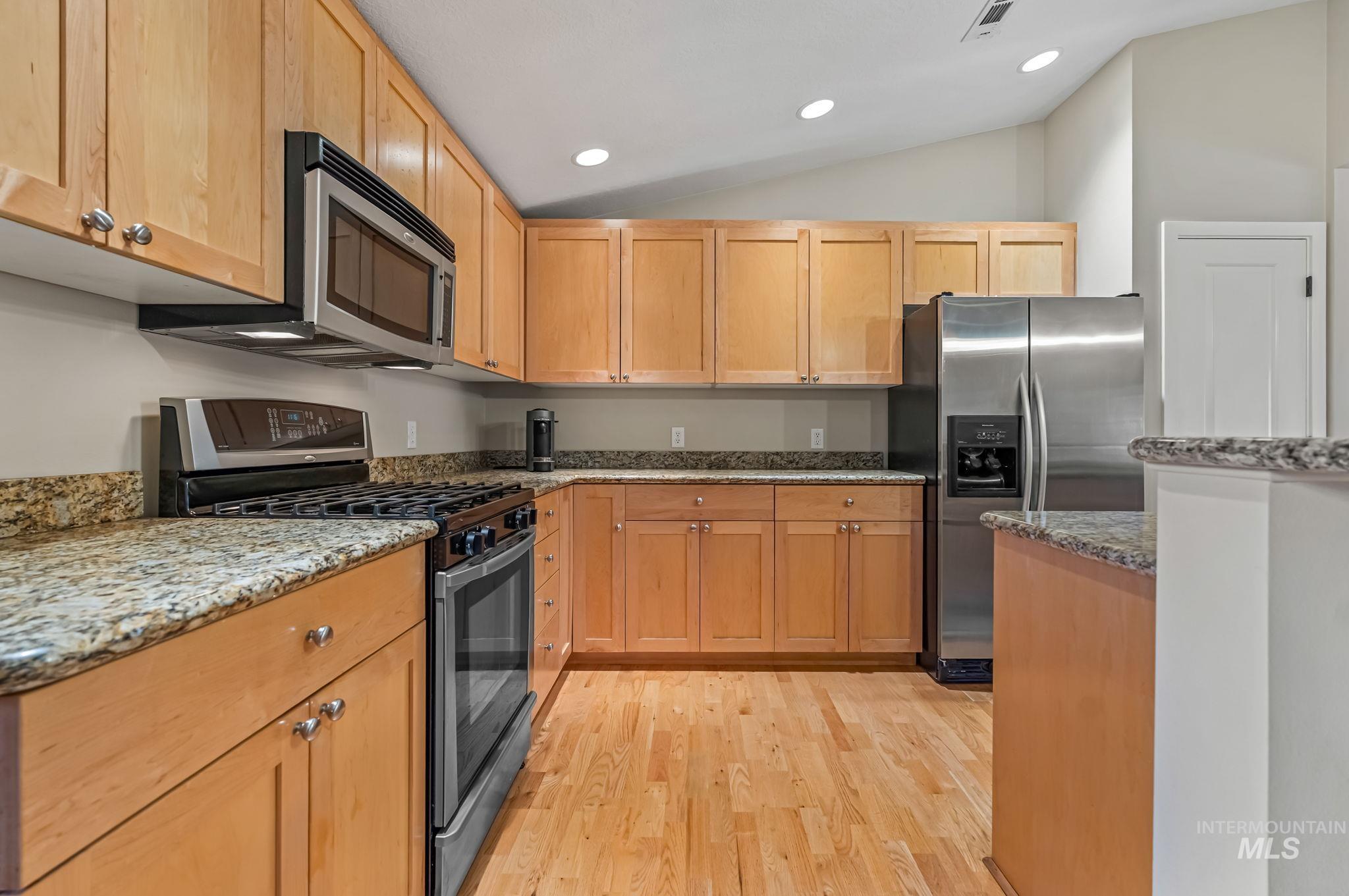 Kitchen with stainless steel appliances, granite counters, recessed lighting, lofted ceiling, and light hardwood flooring