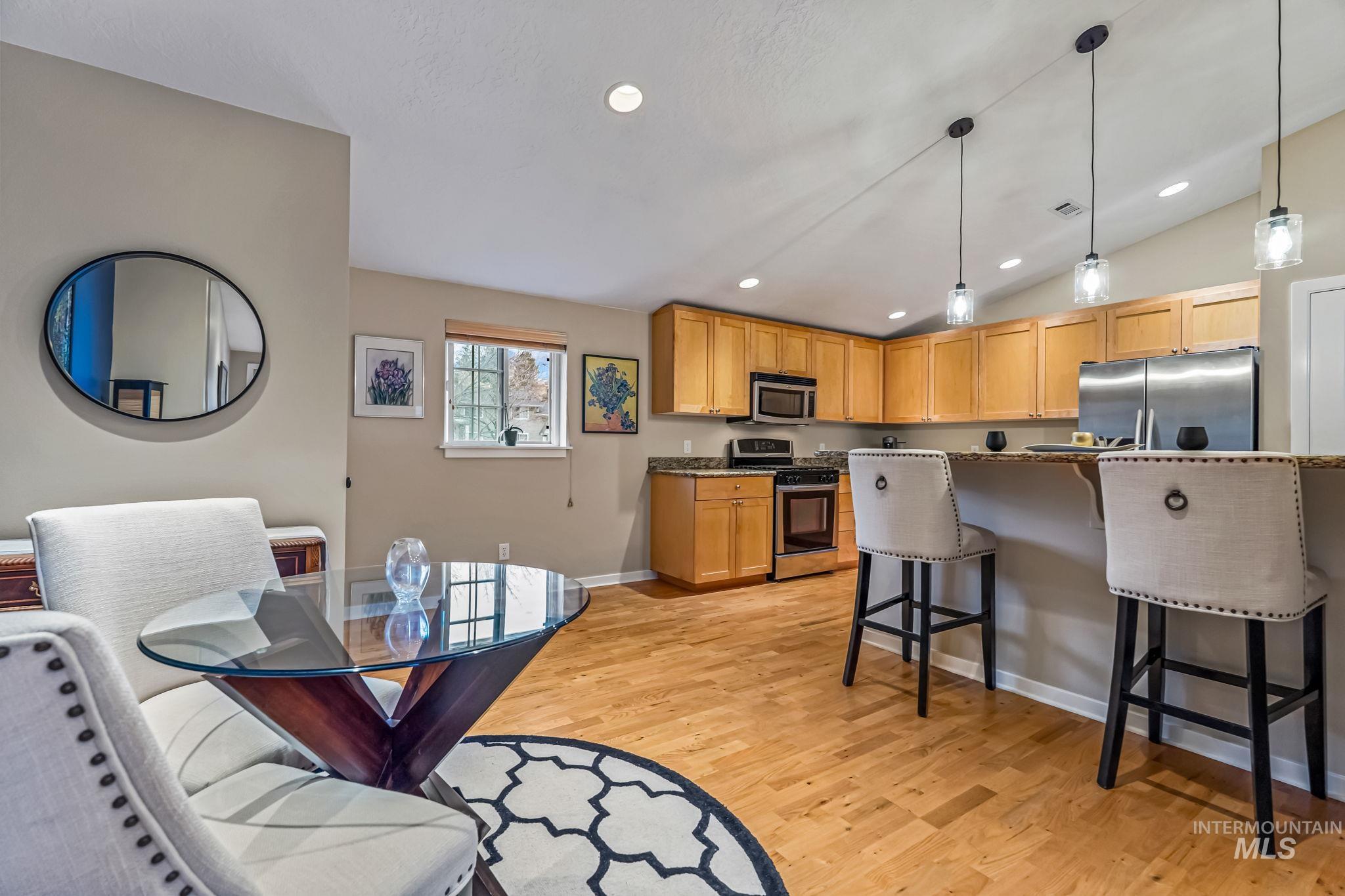 Kitchen with a kitchen bar, stainless steel appliances, light hardwood flooring, decorative light fixtures, and vaulted ceiling