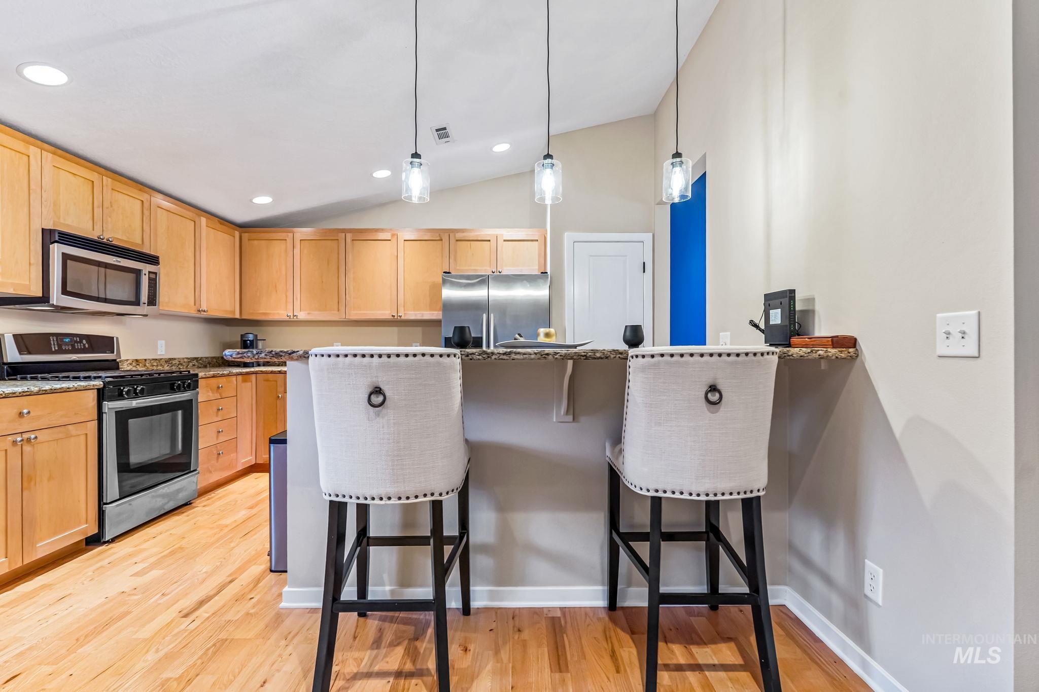 Kitchen with a breakfast bar area, stainless steel appliances, light wood finish cabinets, a peninsula, and vaulted ceiling