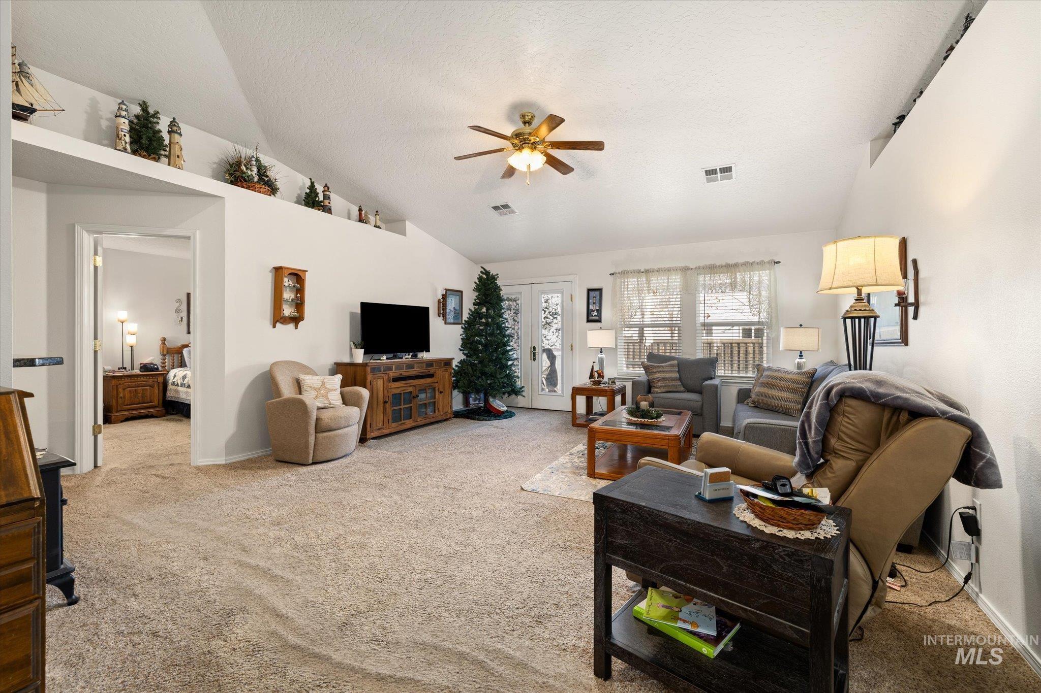 Living area featuring light colored carpet, vaulted ceiling, a ceiling fan, and a textured ceiling