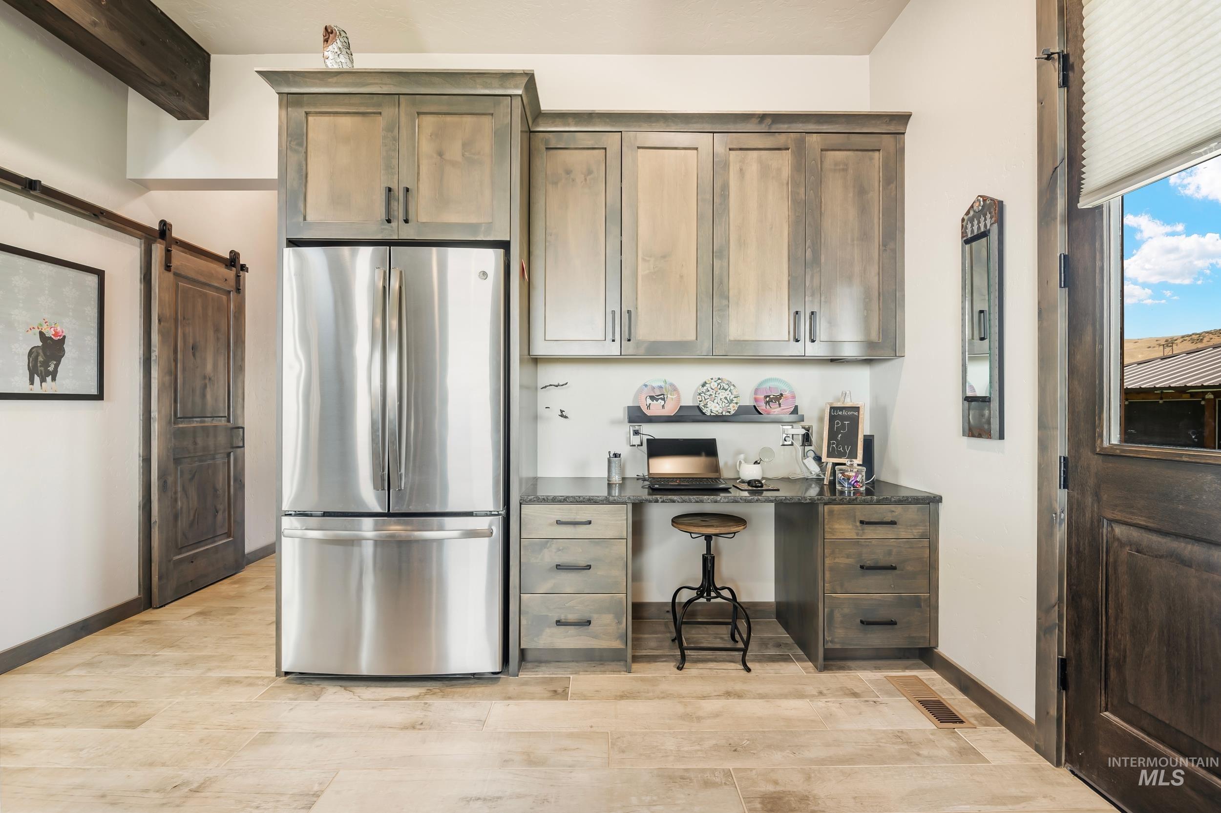 Kitchen with freestanding refrigerator, light wood-type flooring, built in study area, a barn door, and beamed ceiling