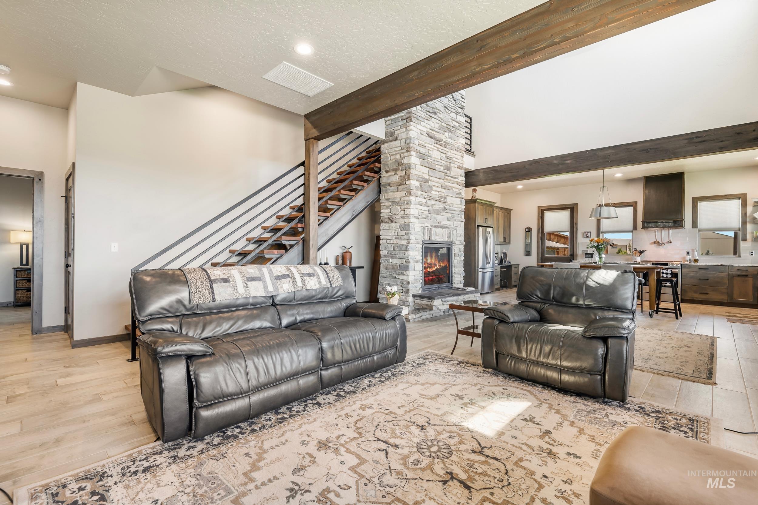 Living room with a fireplace, beam ceiling, light wood-style floors, a towering ceiling, and recessed lighting