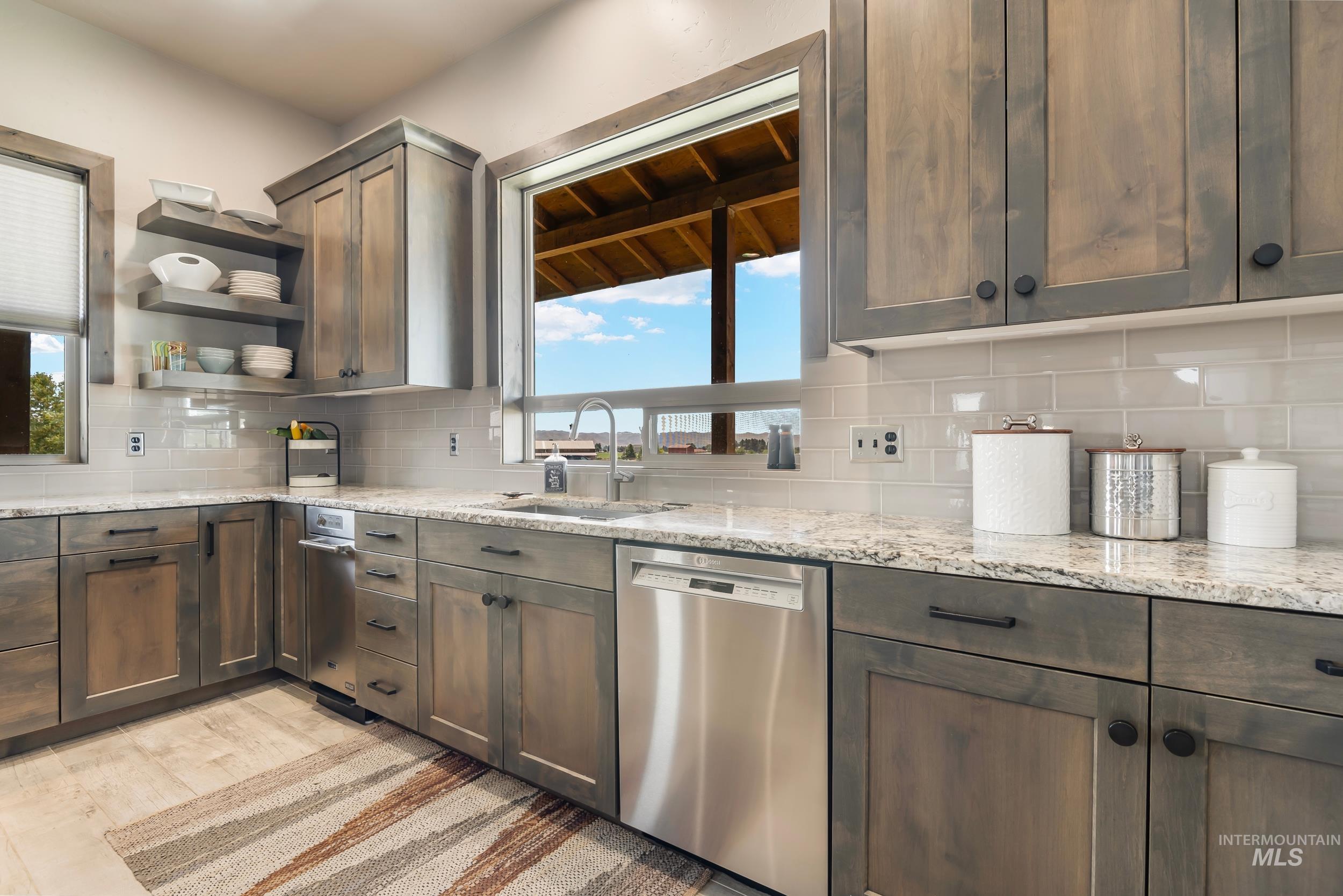 Kitchen featuring stainless steel dishwasher, decorative backsplash, open shelves, light stone countertops, and light wood finished floors