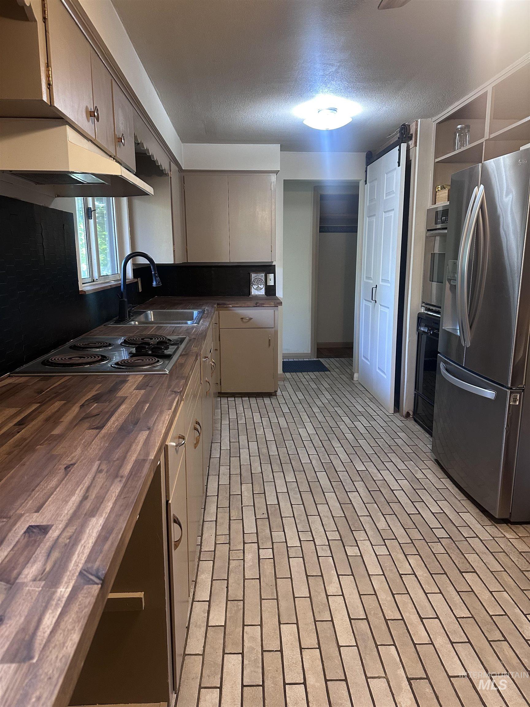 Kitchen with butcher block countertops, appliances with stainless steel finishes, brick patterned floors, open shelves, and under cabinet range hood